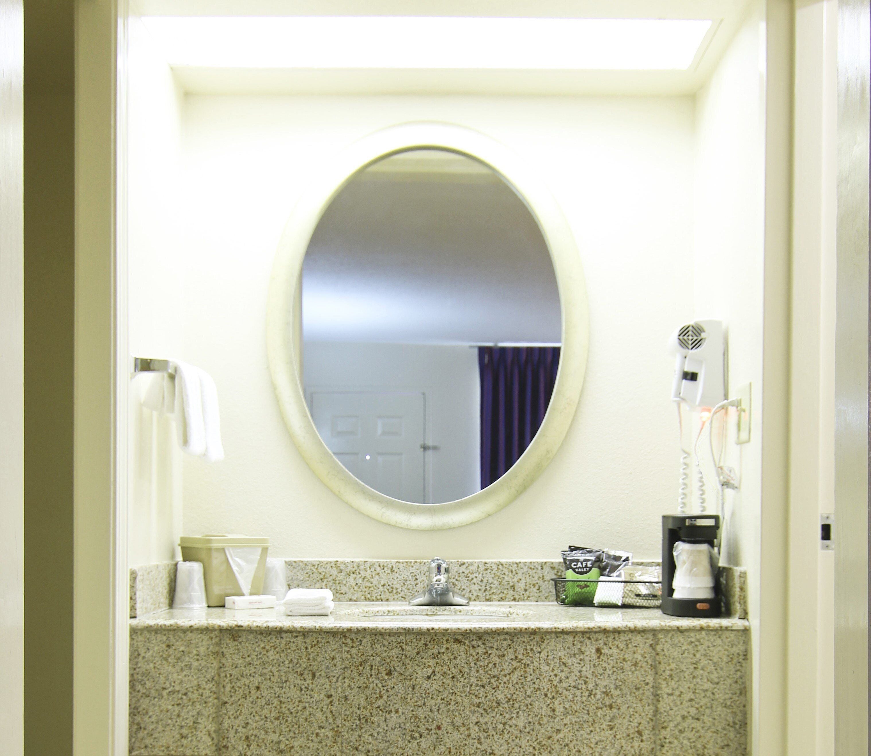 A bathroom with a round mirror, a sink, a hairdryer, and a coffee machine.