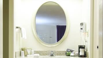A bathroom with a round mirror, a sink, a hairdryer, and a coffee machine.