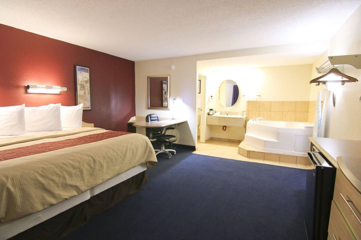A hotel room with a bed, desk, chair, and a bathroom with a bathtub.