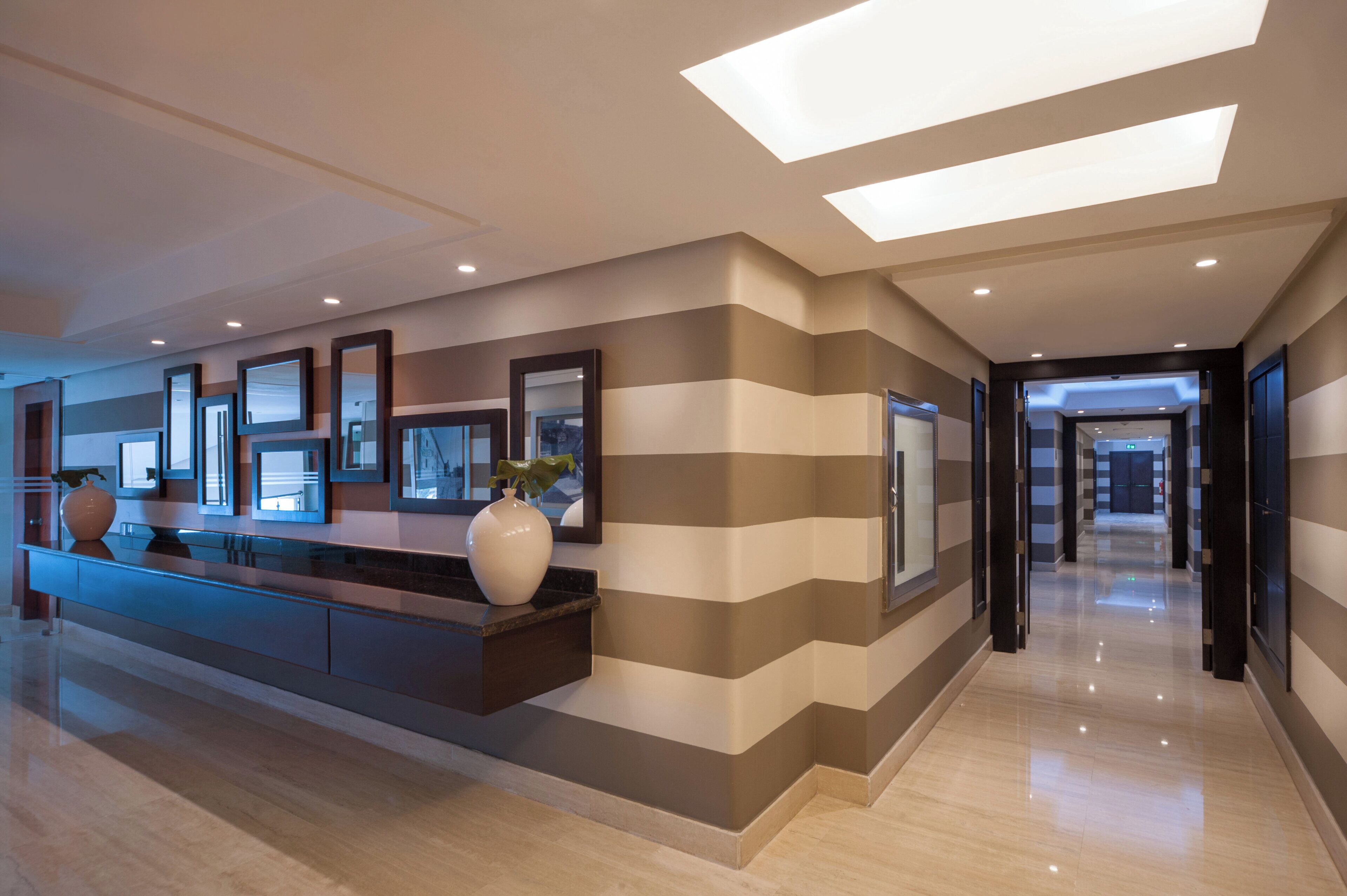 A hotel lobby with a reception desk, framed artwork, and a large vase.