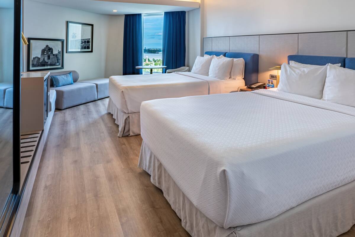 Une chambre d’hôtel avec deux lits, un canapé, une table et une vue sur la ville.