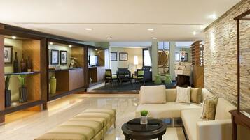 A modern hotel lobby with a seating area, a reception desk, and a wall with a ship model.