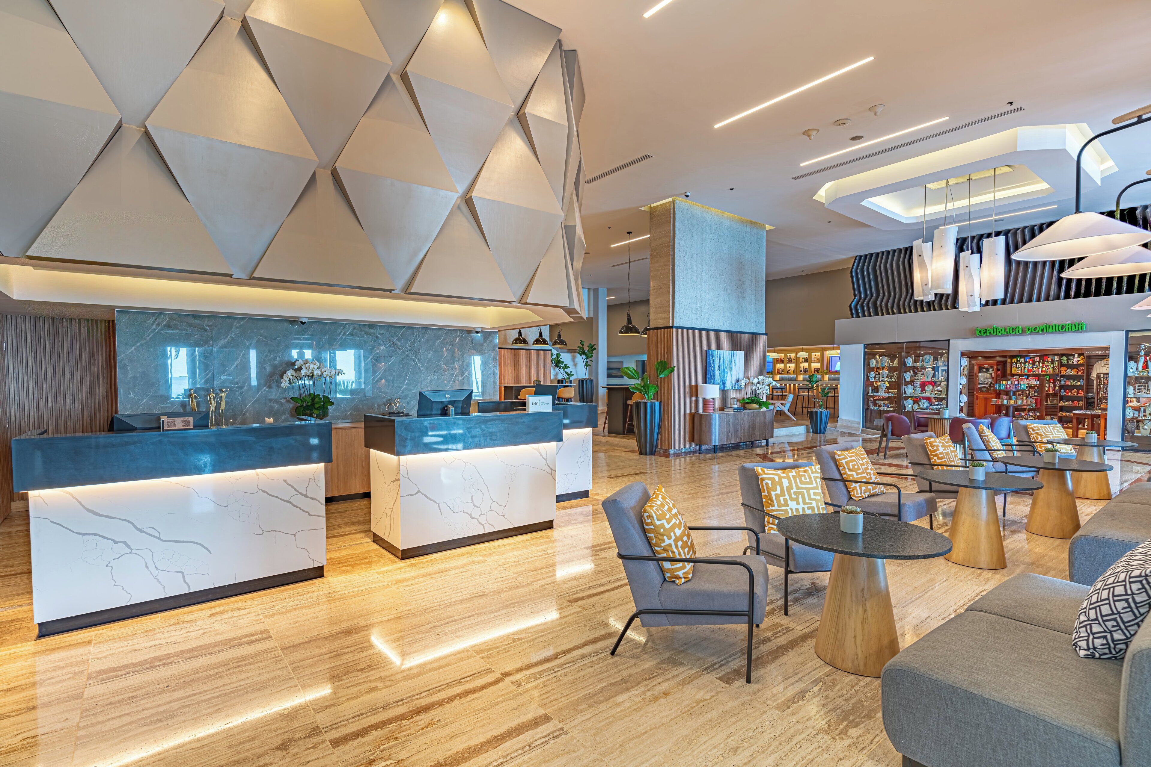 A modern hotel lobby with a reception desk, seating area, and a visible store named 'República Dominicana'.