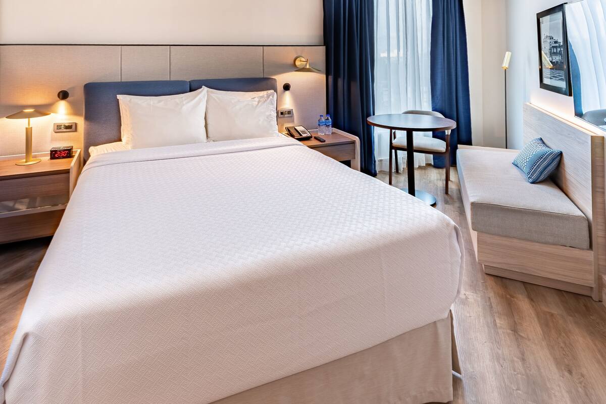 Une chambre d’hôtel avec un grand lit, des tables de chevet, une petite table ronde et un canapé.