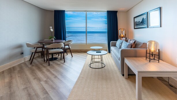 Ein modernes Wohnzimmer mit Meerblick, einem runden Esstisch, einer Couch und einem kleinen Beistelltisch.