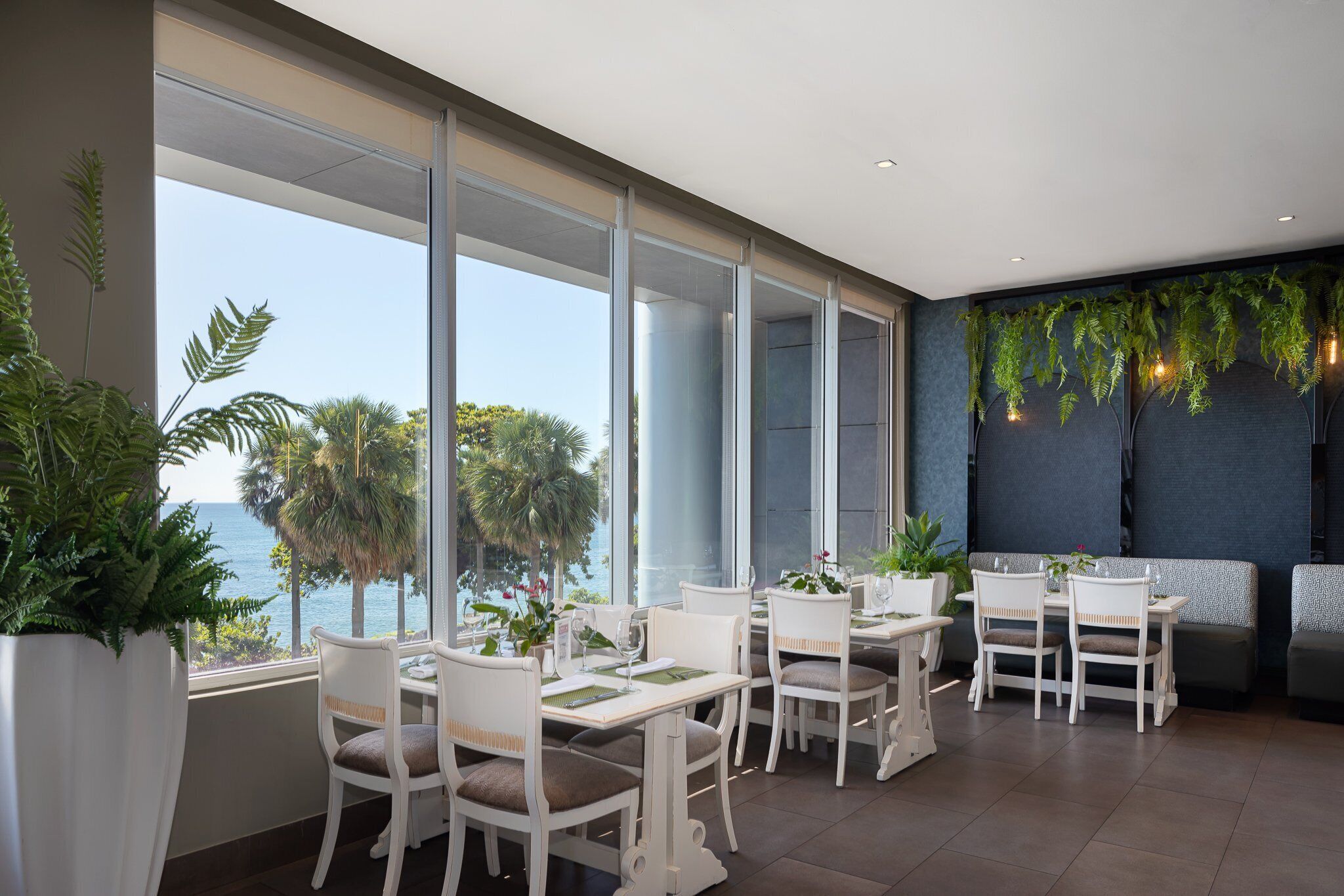 A restaurant with white furniture and large windows overlooking the ocean.