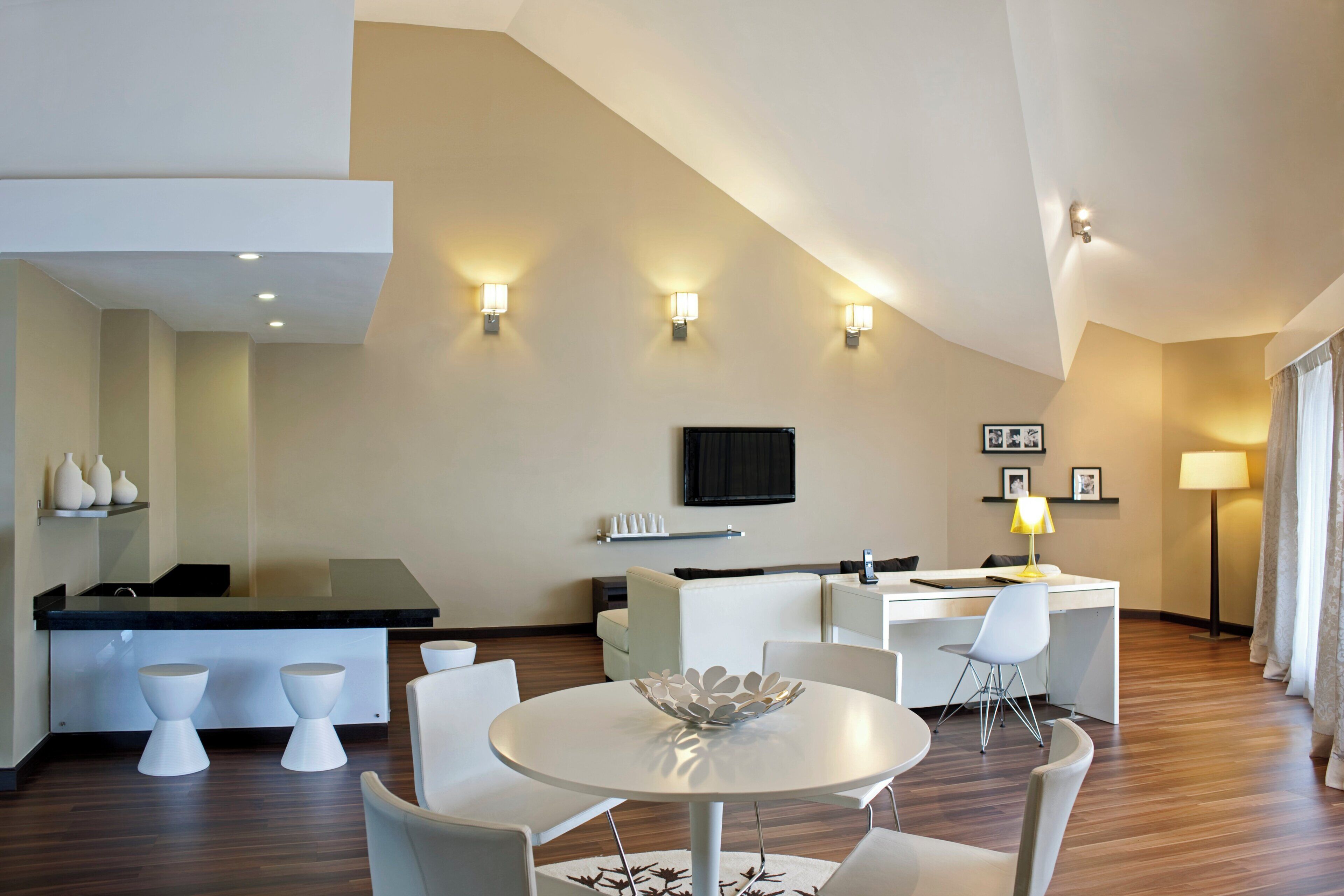 Een moderne hotelkamer met een zithoek, een flatscreen televisie aan de muur en een groot raam met gordijnen.