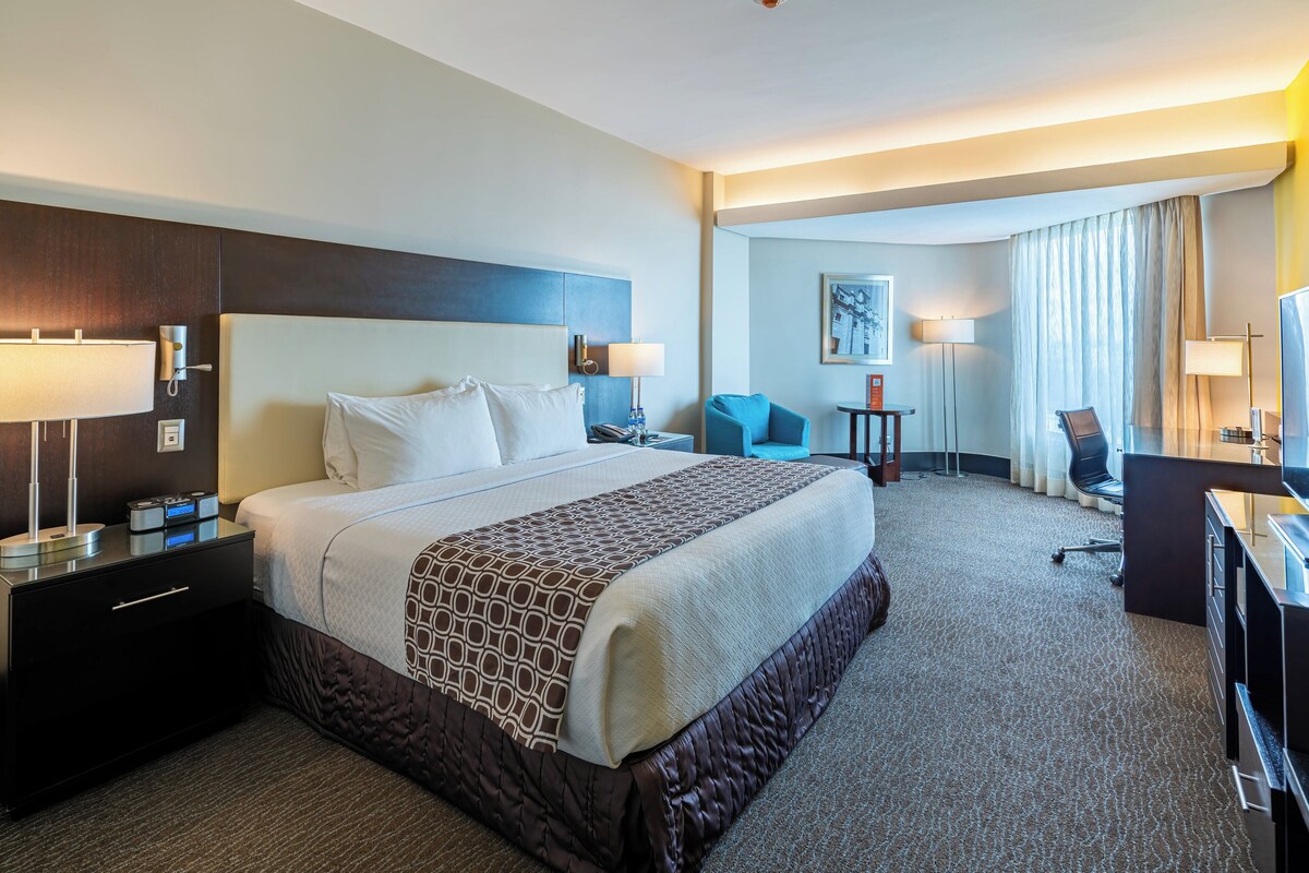 Ein Hotelzimmer mit einem großen Bett, einem Schreibtisch, einem Stuhl und einer Schreibtischlampe.