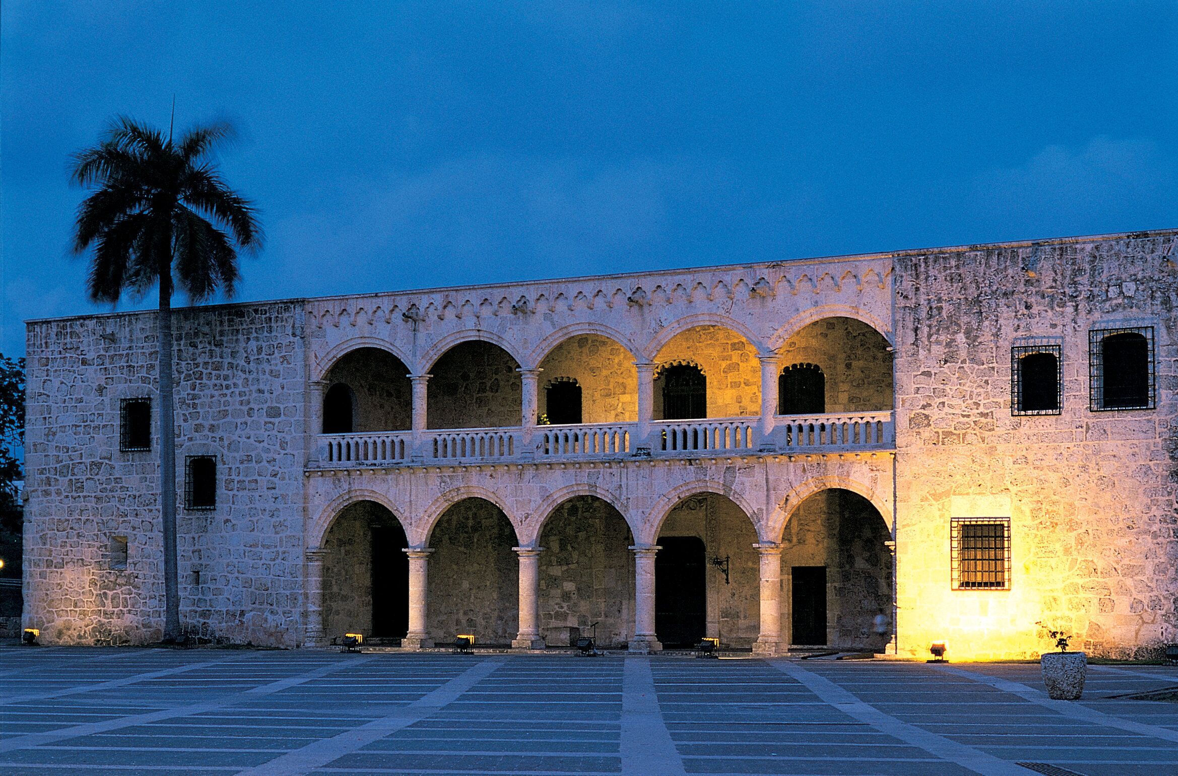 A historic building with a central courtyard, multiple arches, and a palm tree.