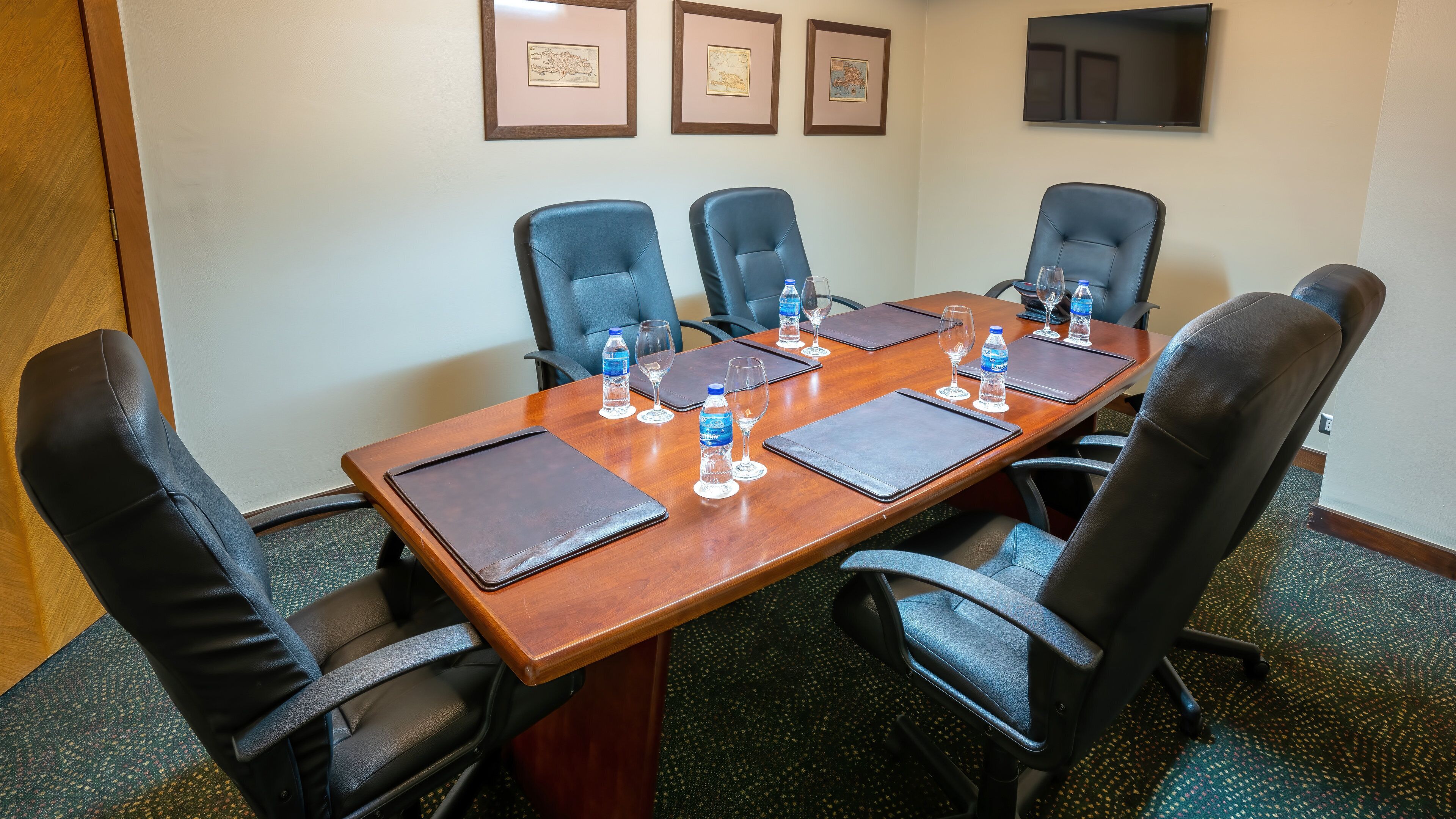 A conference room with a wooden table, six black leather chairs, water bottles, and wine glasses on place settings.