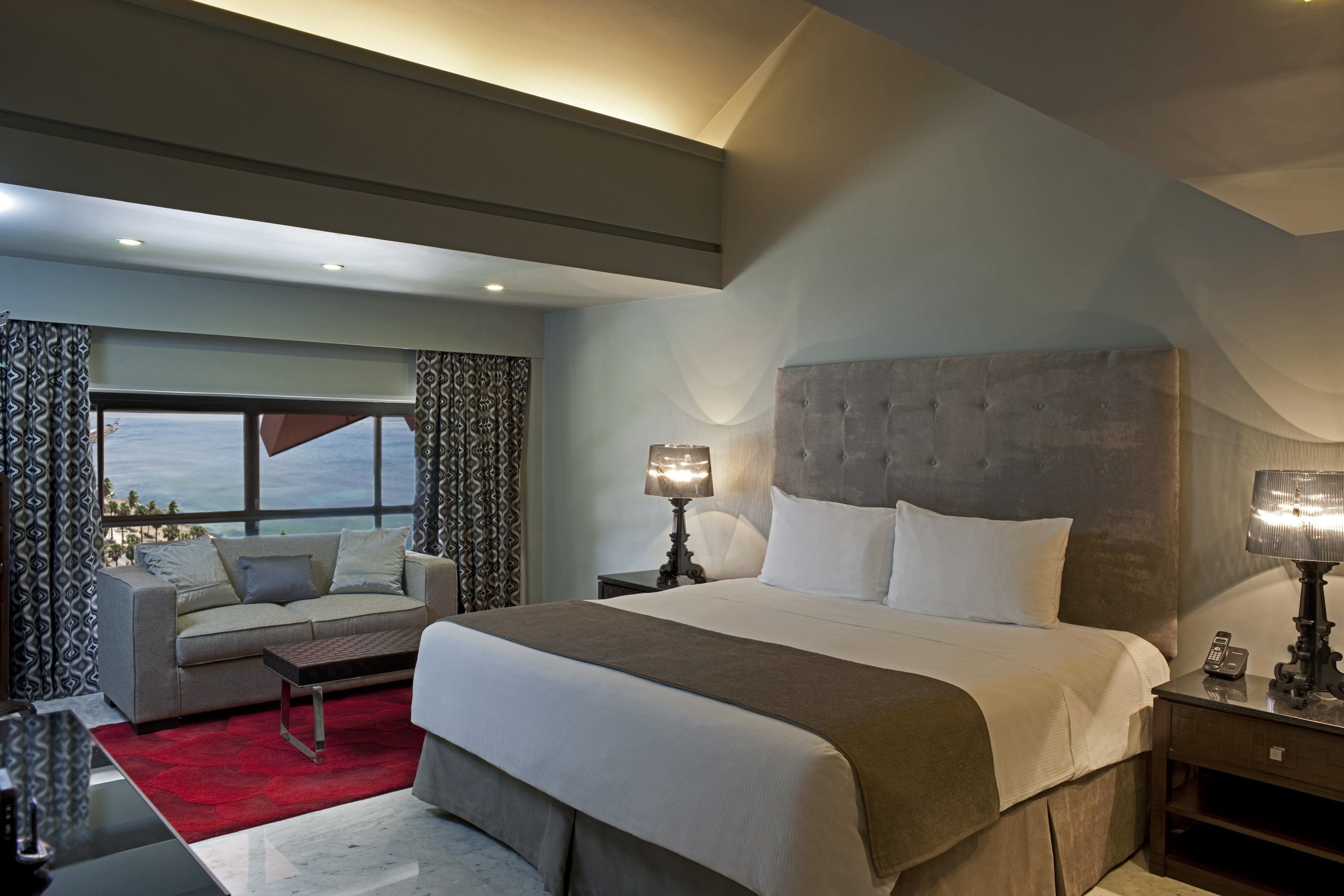 Une chambre d’hôtel moderne, dotée d’un grand lit, d’un canapé et offrant une vue sur l’océan.