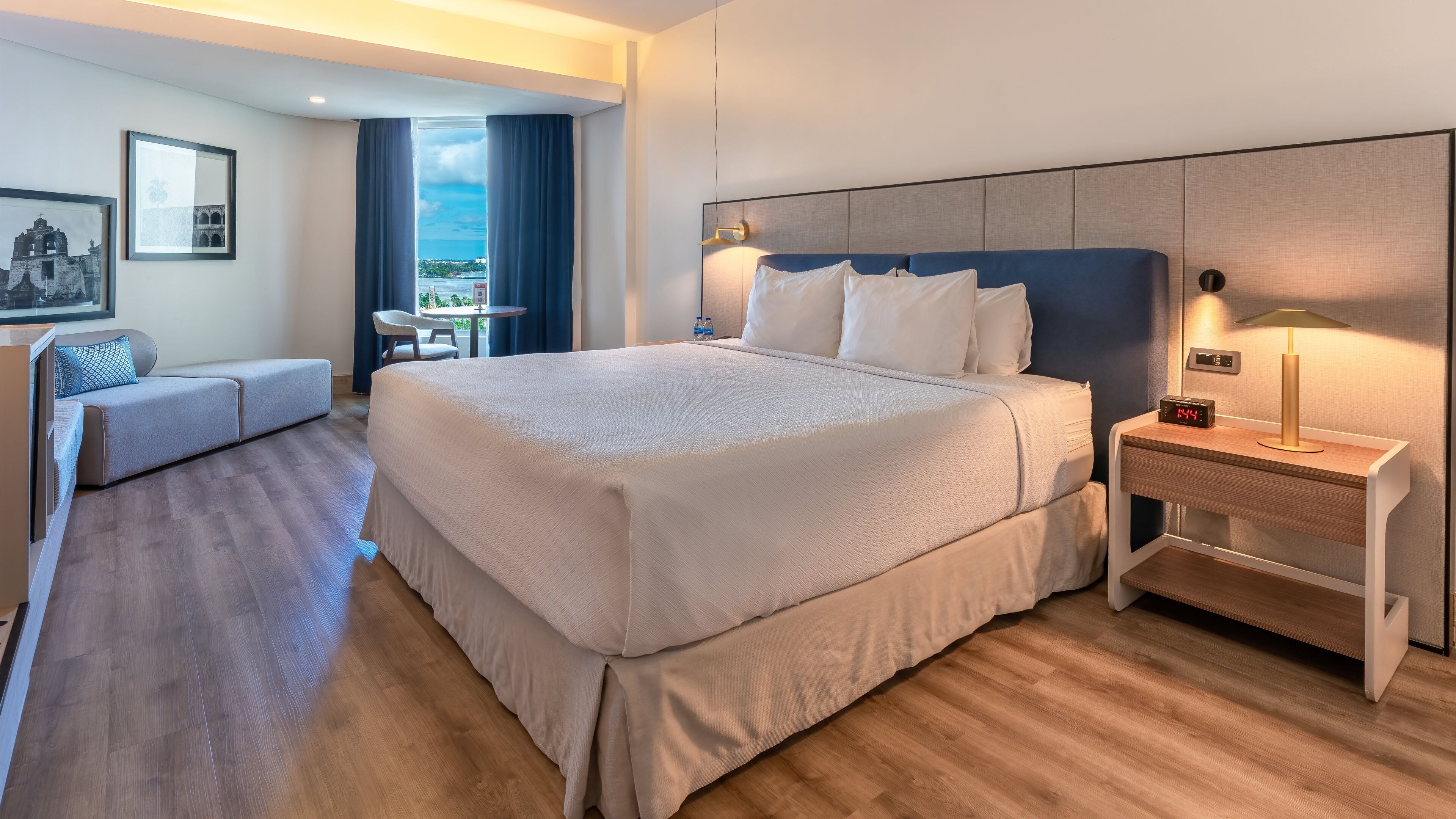 A hotel room with a large bed, bedside table, and a view of the sea.