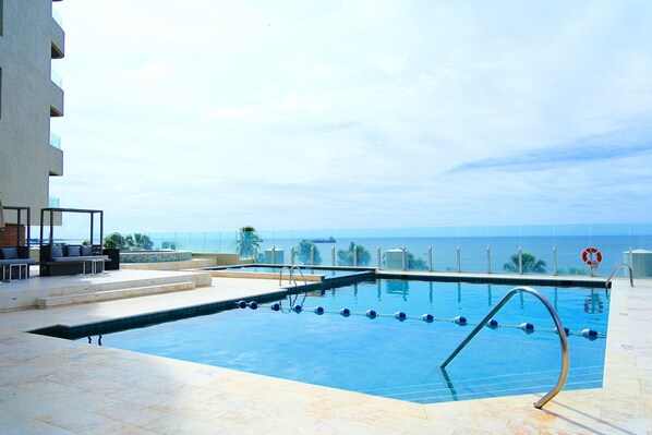 A swimming pool with a view of the ocean, a lifebuoy, and a seating area with chairs and a table.