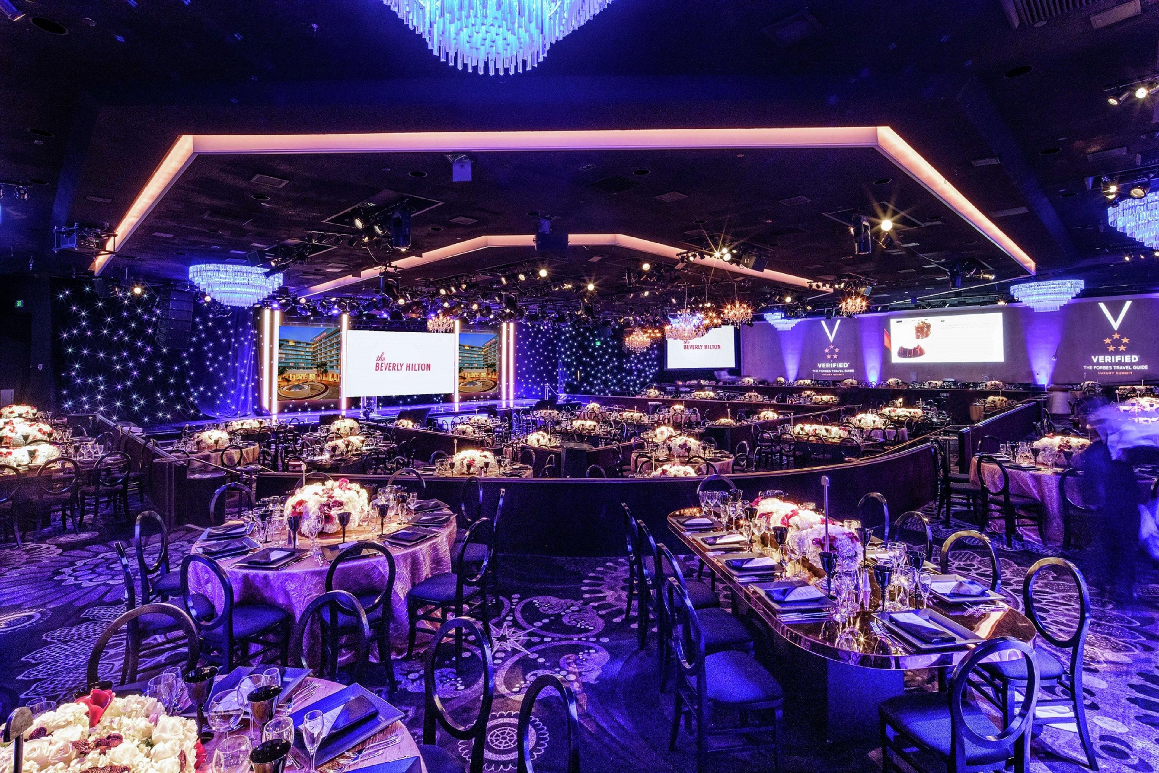 A banquet hall with round tables set for dining, a stage with a large screen, and a VIP section with a 'Verified' sign.