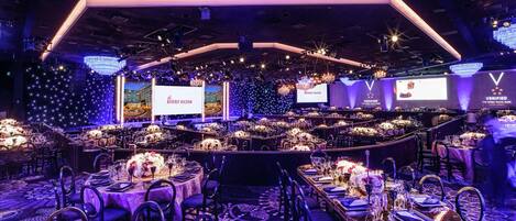 A banquet hall with round tables set for dining, a stage with a large screen, and a VIP section with a 'Verified' sign.