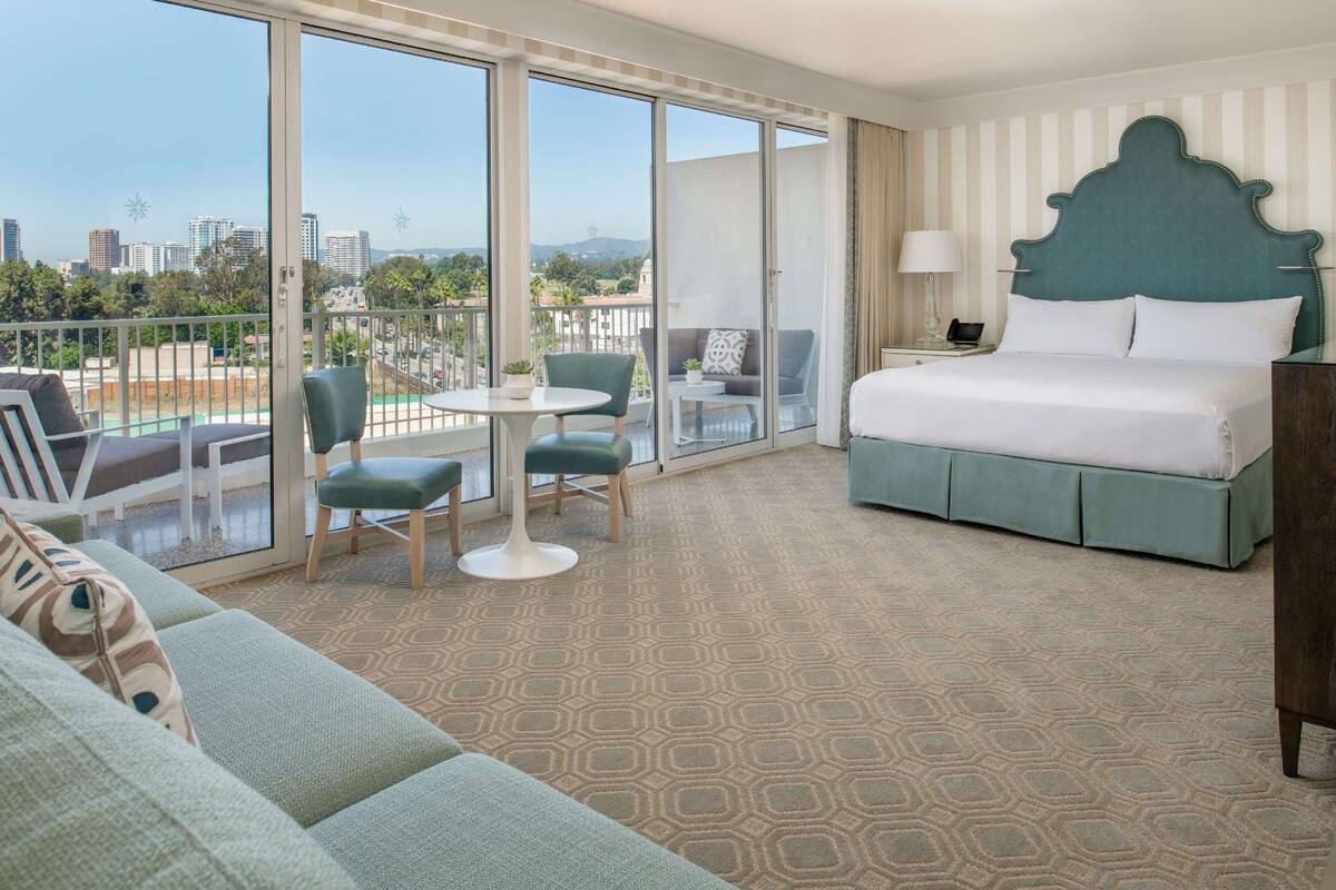Une chambre d’hôtel avec un grand lit, un balcon avec des sièges et une vue sur la ville.