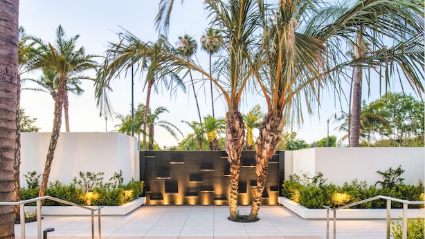 A modern outdoor area with palm trees, a geometric wall, and metal railings. - The Beverly Hilton (Beverly Hills)