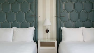 A hotel room with two beds, a nightstand with a lamp, and a striped wall.
