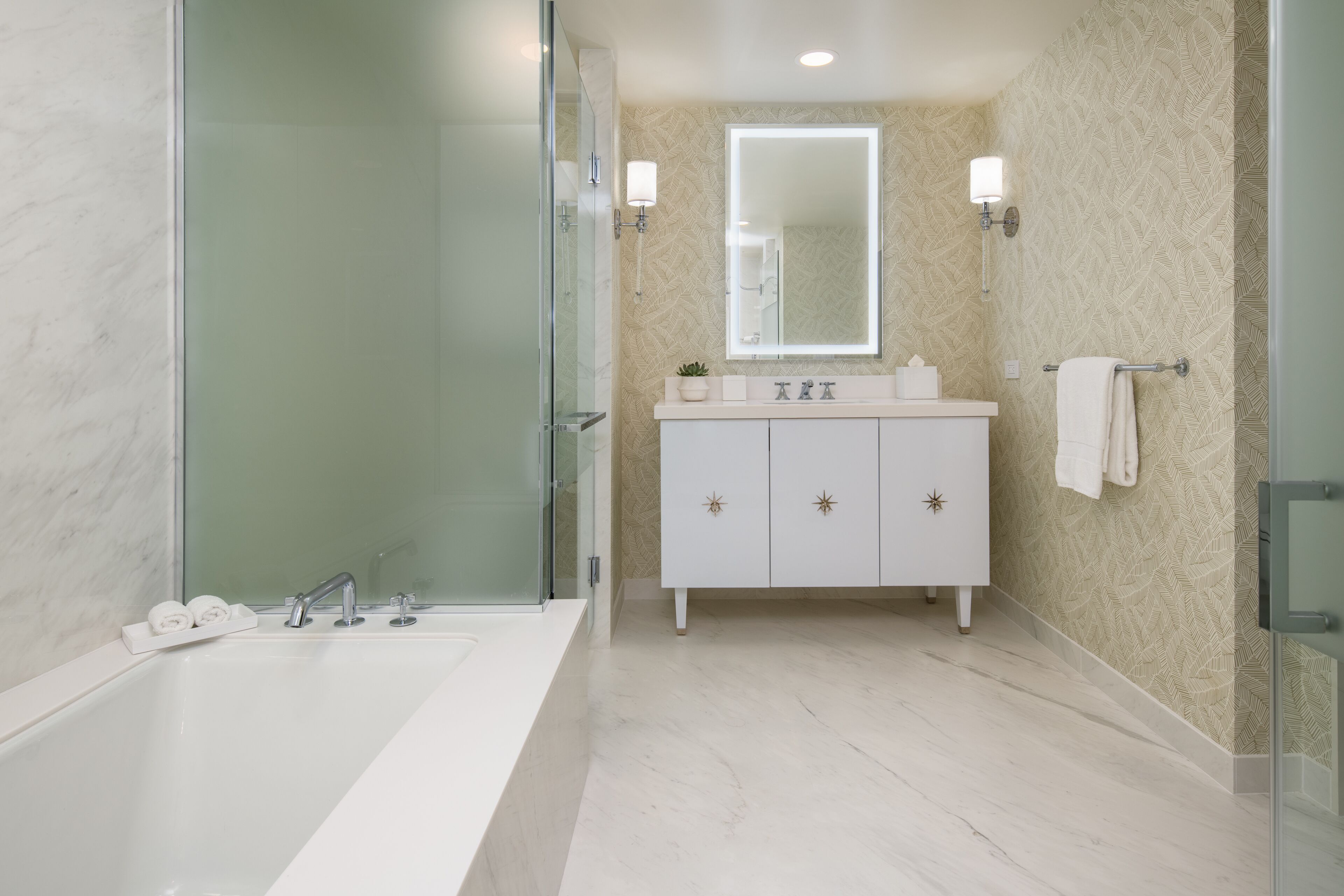 A modern bathroom with a glass-enclosed shower, a large white bathtub, a vanity with a mirror, and a towel rack.
