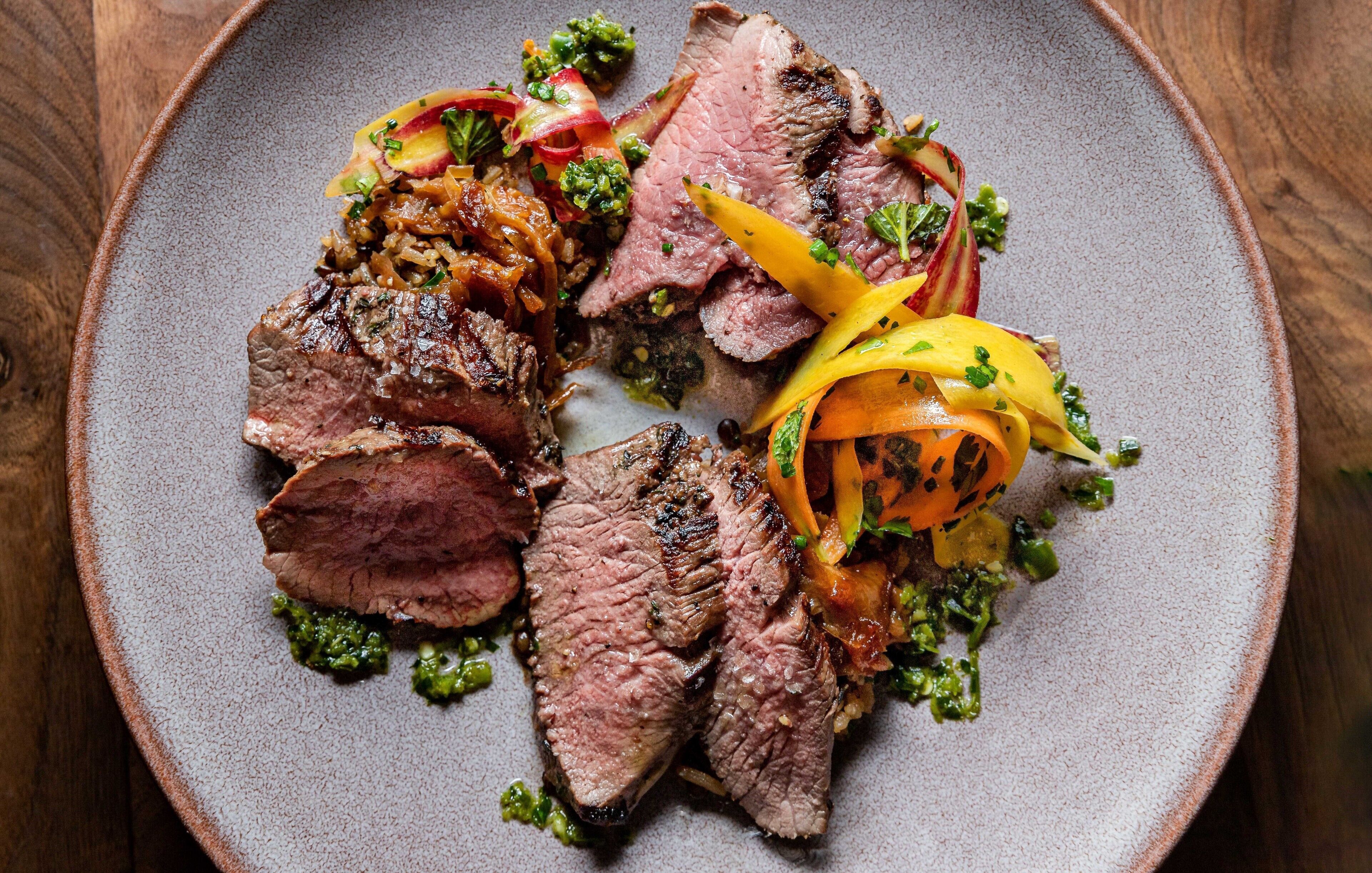 A plate of sliced steak with vegetables and a green sauce.