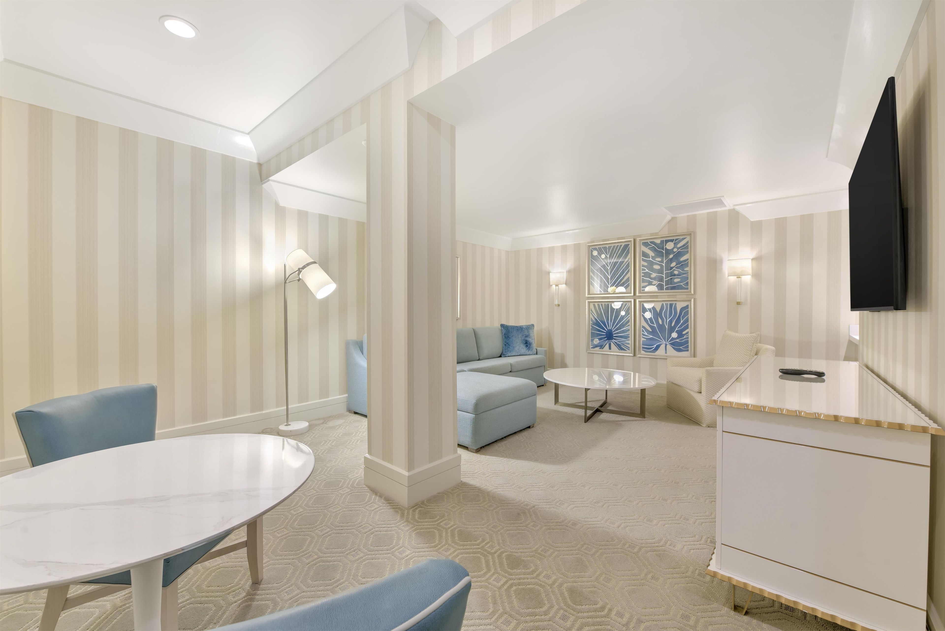 A hotel room with a dining table, a sofa, a TV, and a patterned carpet.