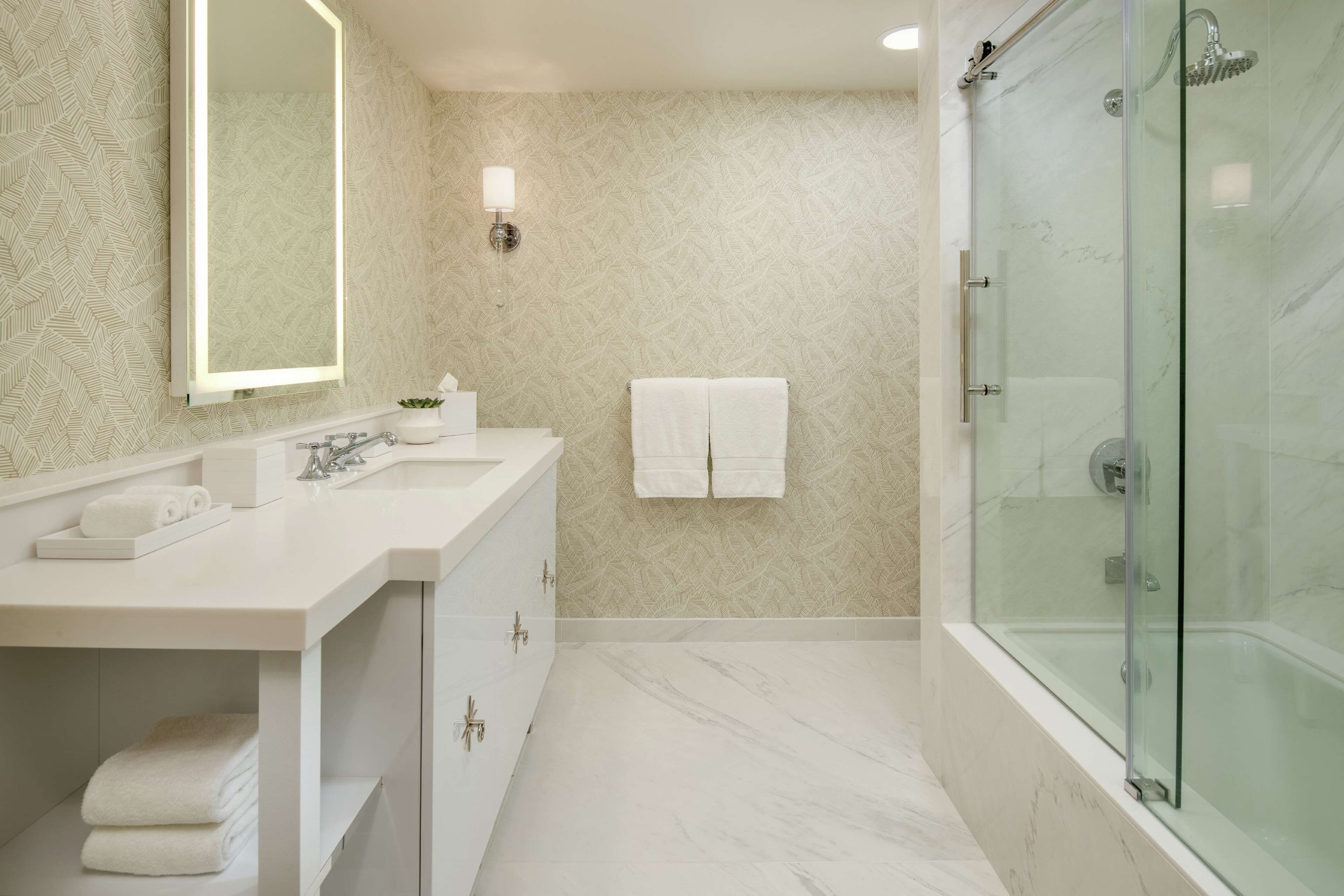 A modern bathroom with a large mirror, white vanity, and a glass-enclosed shower.