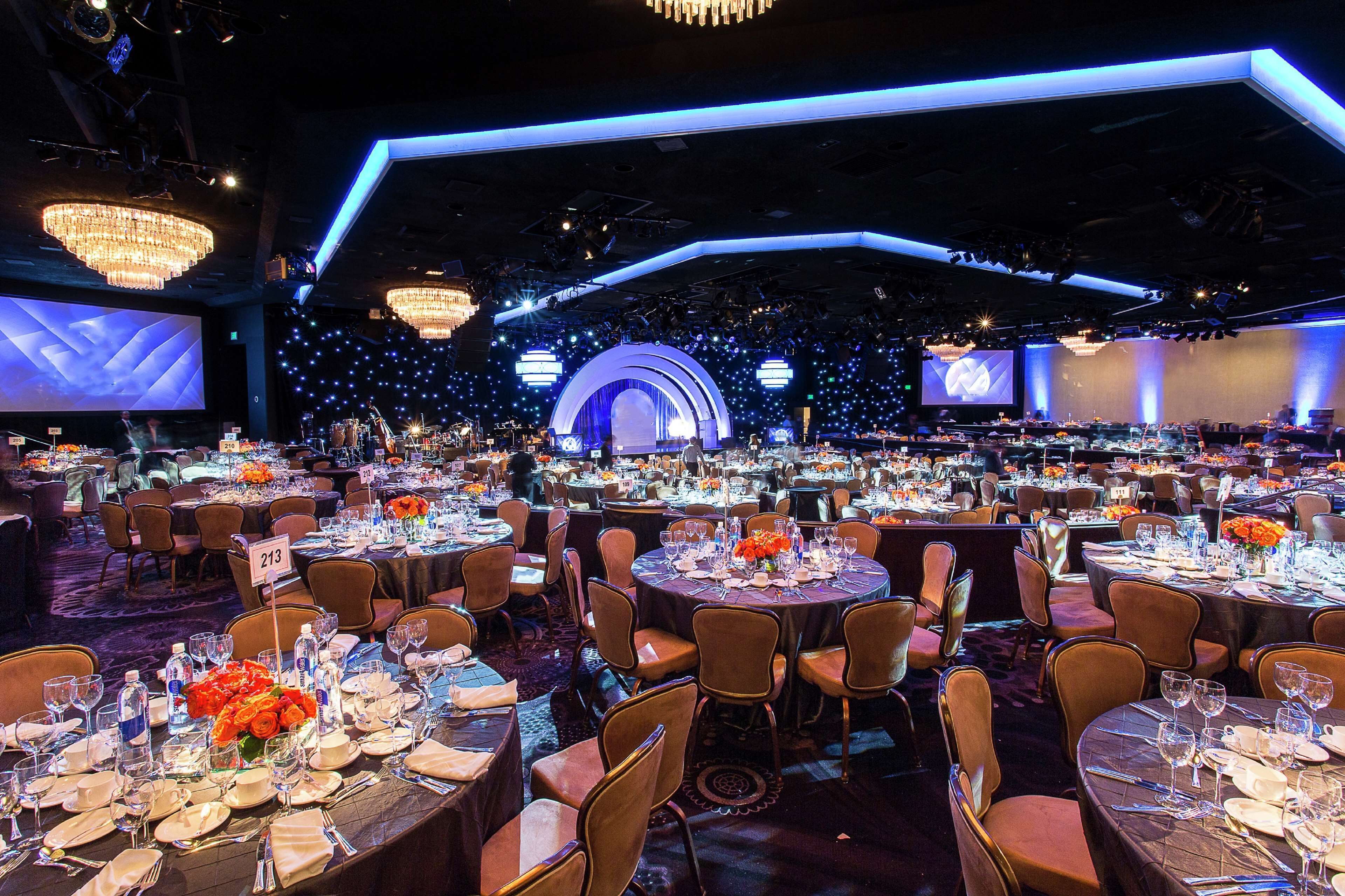 A banquet hall with round tables set for dining, a stage with a large screen, and a backdrop of lights.
