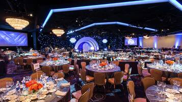 A banquet hall with round tables set for dining, a stage with a large screen, and a backdrop of lights.