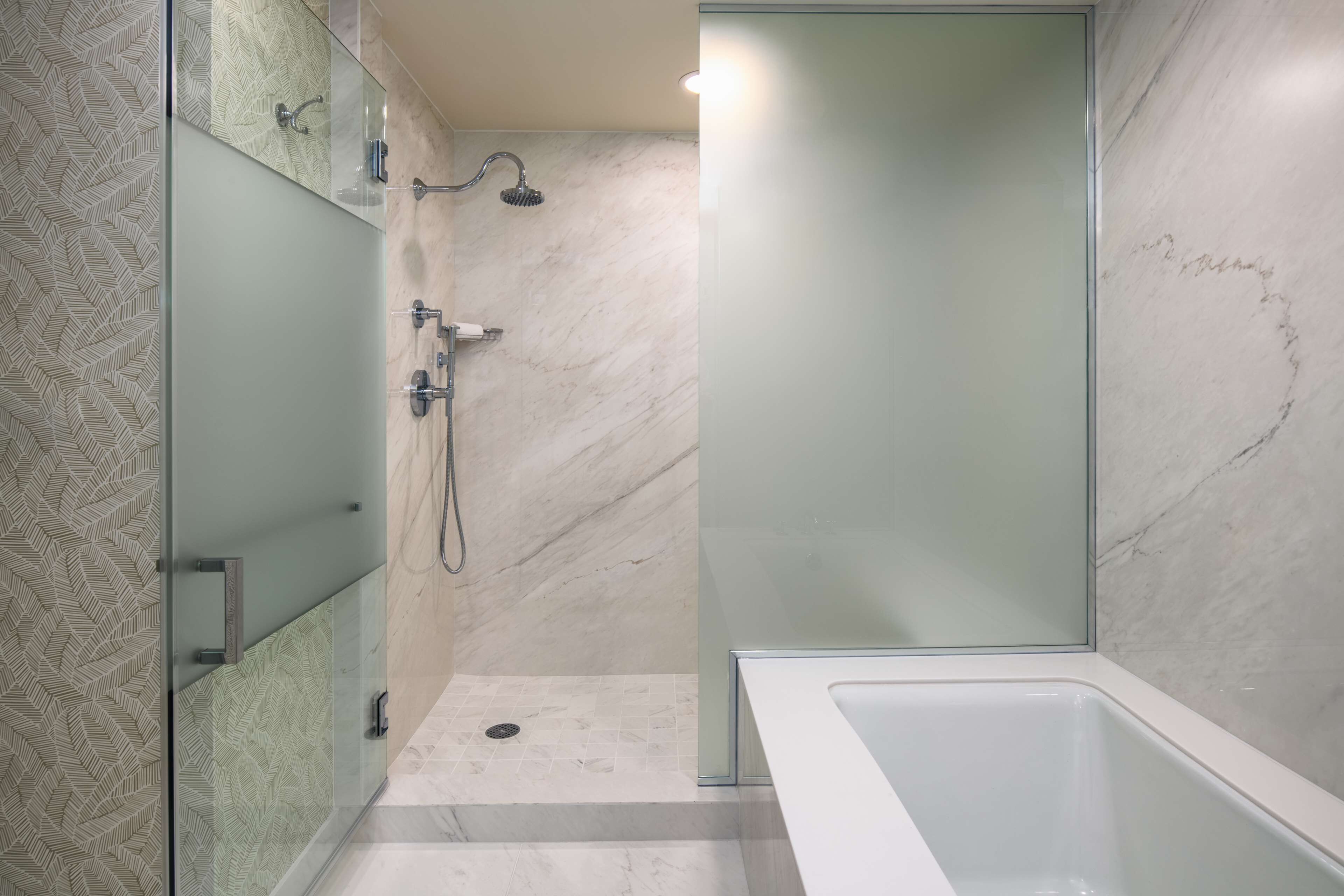 A modern bathroom with a glass shower enclosure, a bathtub, and a patterned tile wall.