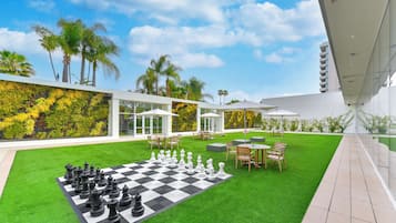 Un espace extérieur aménagé avec un jeu d’échecs, des tables, des chaises et des parasols.