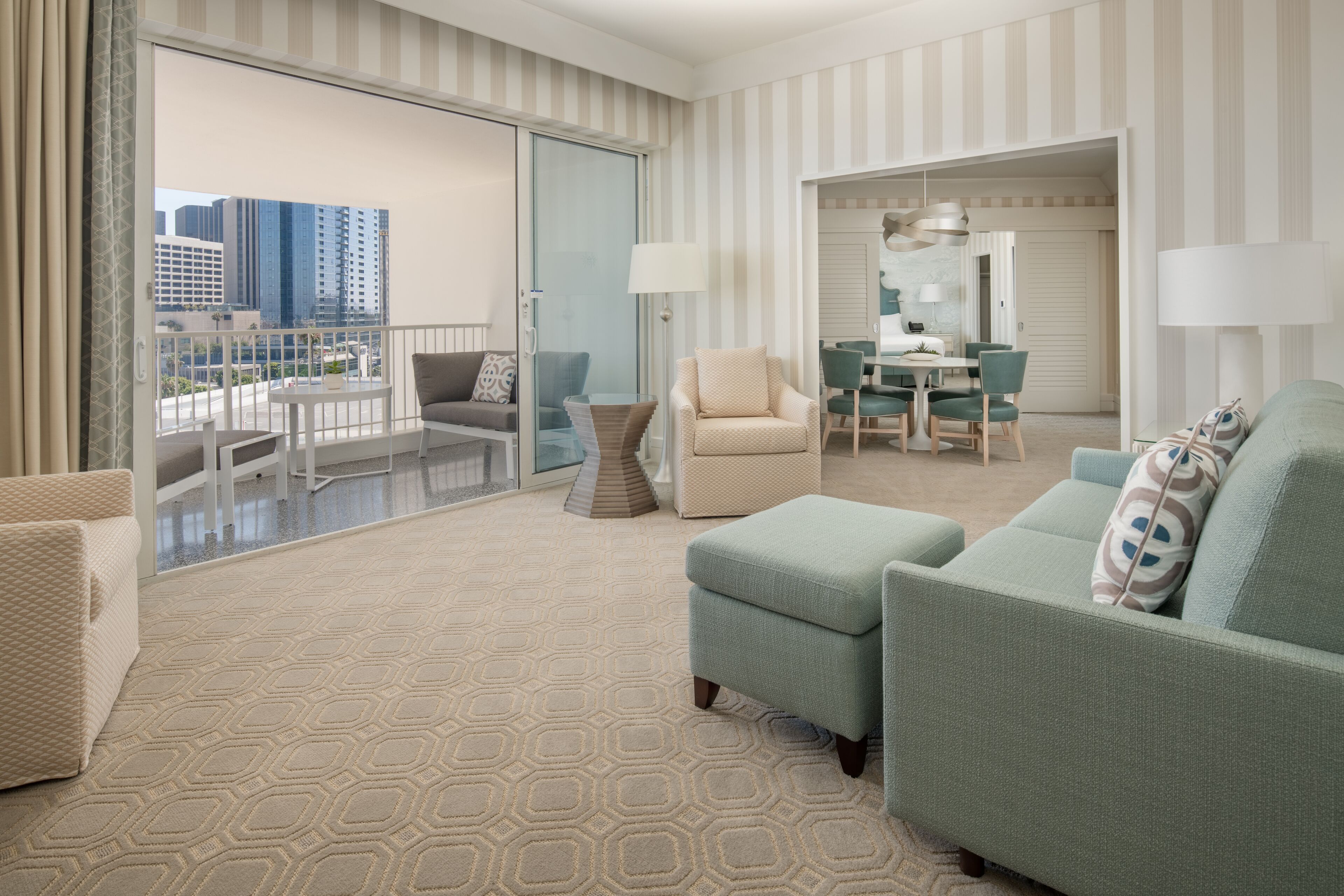 Una habitación de hotel con balcón, zona de comedor y sala de estar con sofá y sillón.