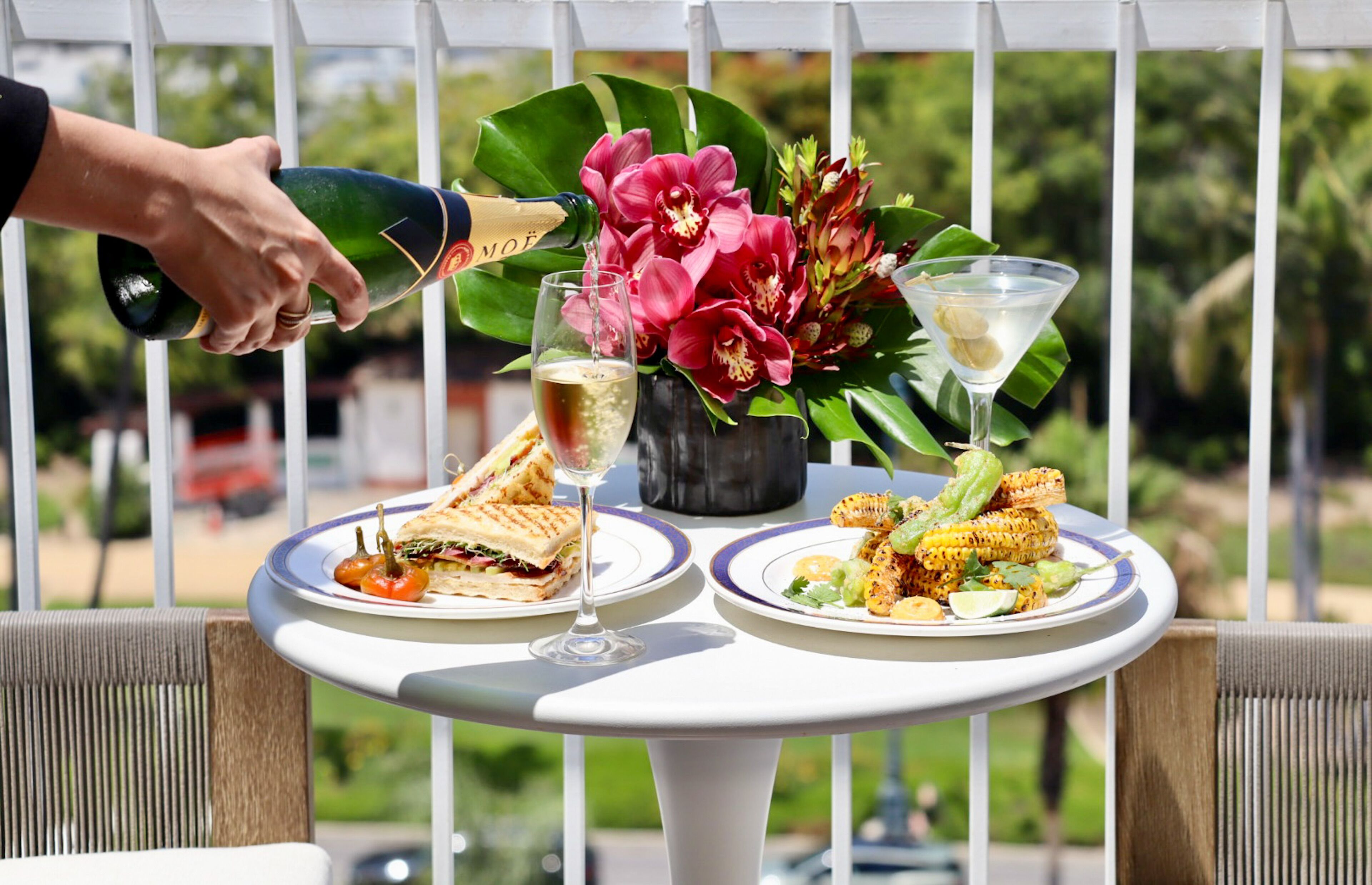 Una mesa con un sándwich, una copa de vino y una copa de martini con un cóctel.