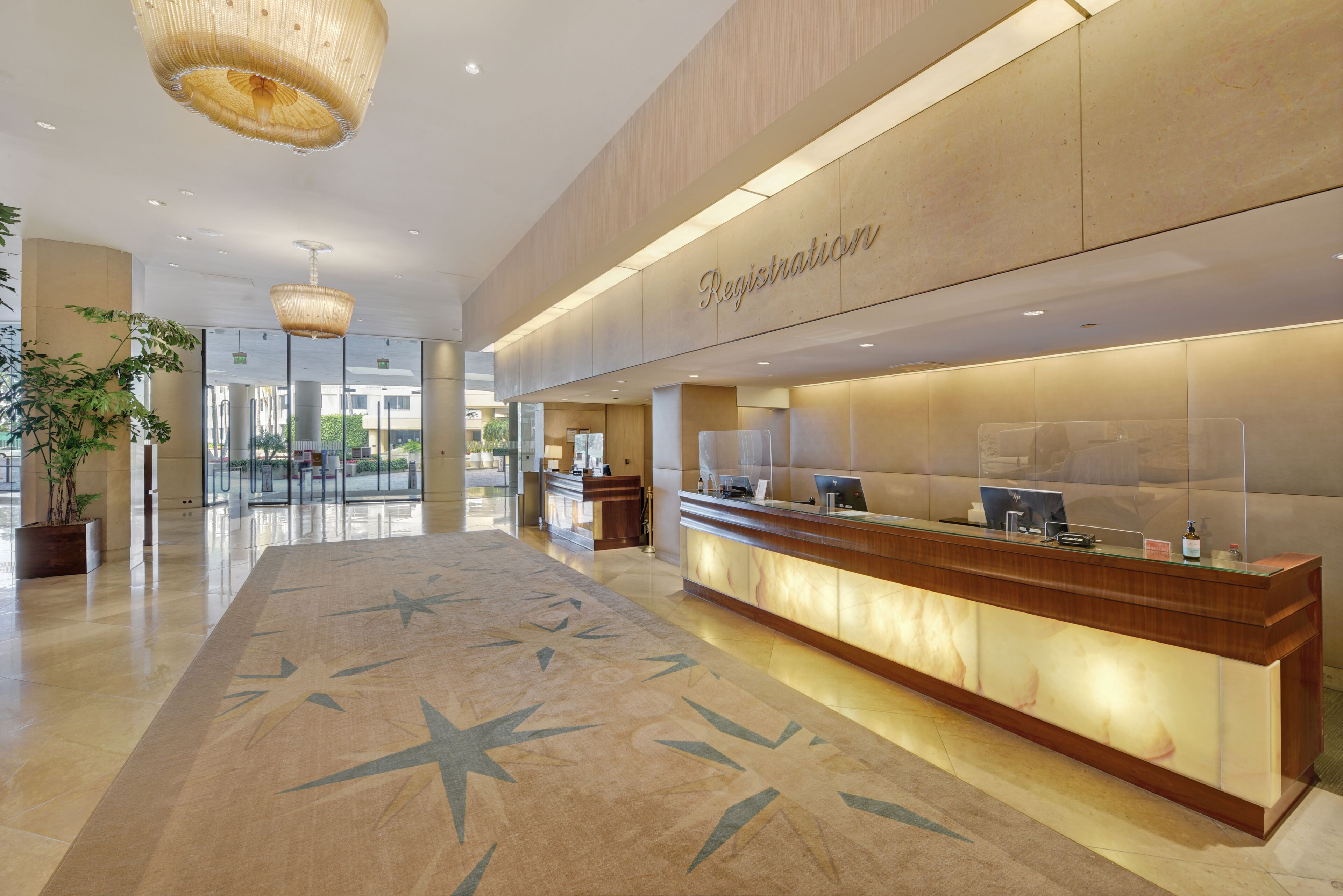 A hotel reception area with a registration desk, a large star-patterned carpet, and a modern chandelier.