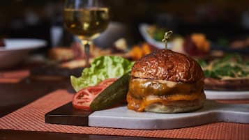A burger with a sesame seed bun, cheese, and a garnish on top, placed on a white plate with a red placemat underneath.