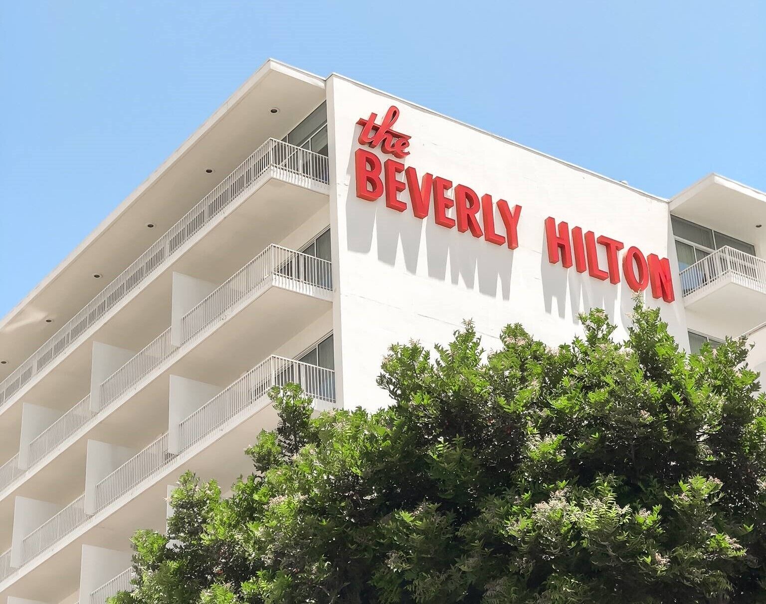 The exterior of the Beverly Hilton hotel with a white facade and red lettering.