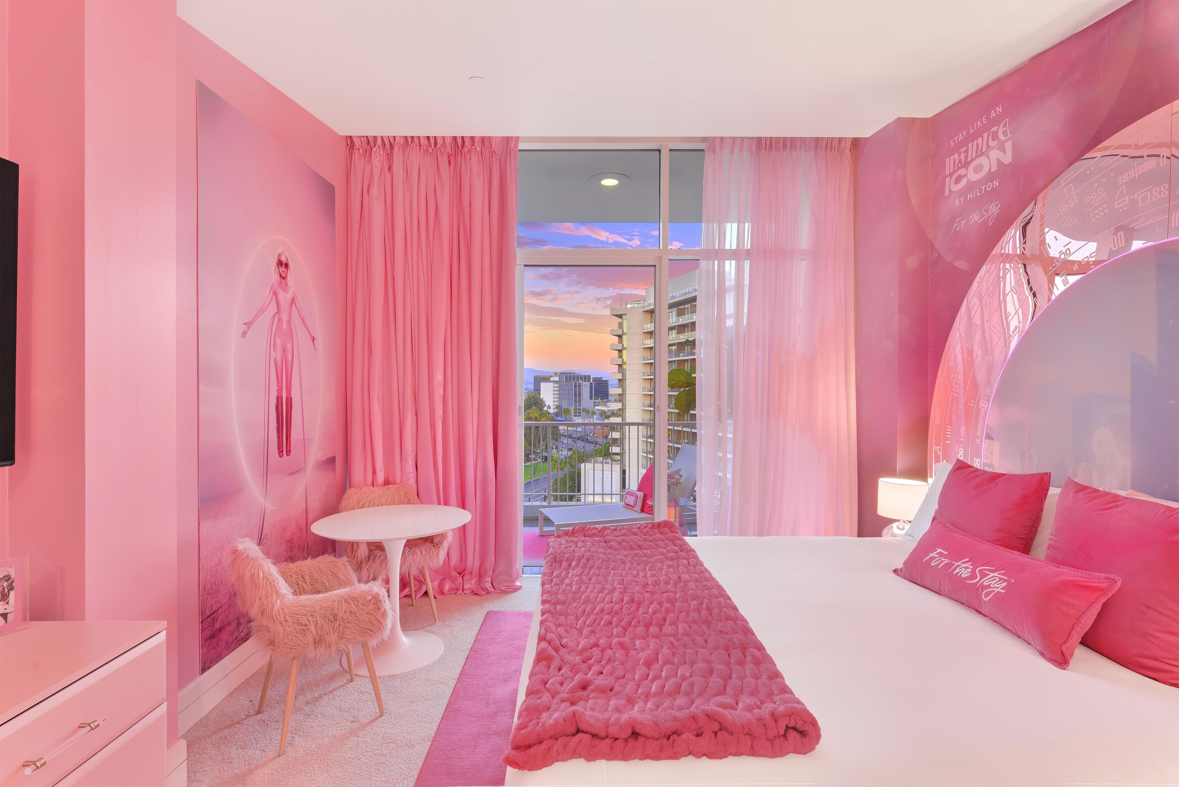 Une chambre d’hôtel décorée dans des tons roses, avec un lit, une table ronde et une vue sur le paysage urbain.