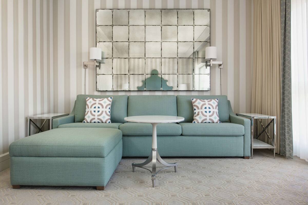 Une pièce avec un canapé vert, une table ronde et un grand miroir au mur.