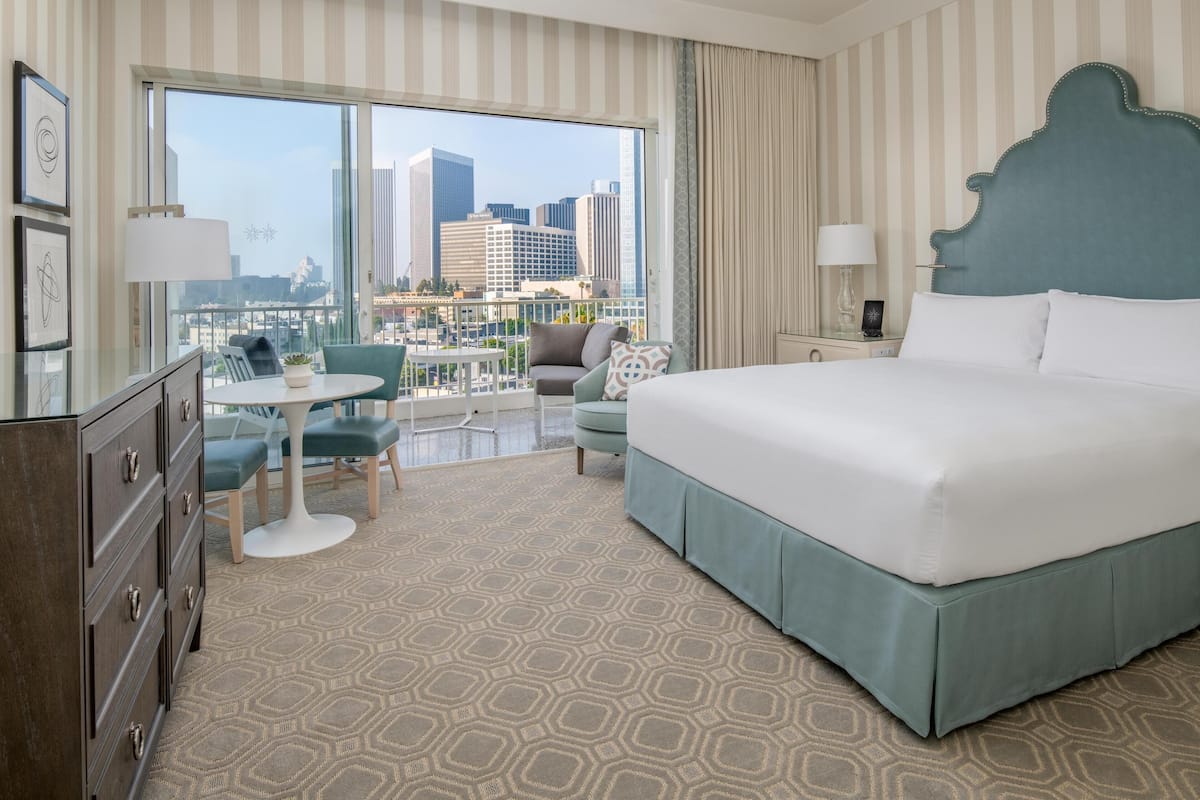 Une chambre d’hôtel avec un grand lit, un balcon offrant une vue sur la ville, un bureau avec une chaise et une commode.