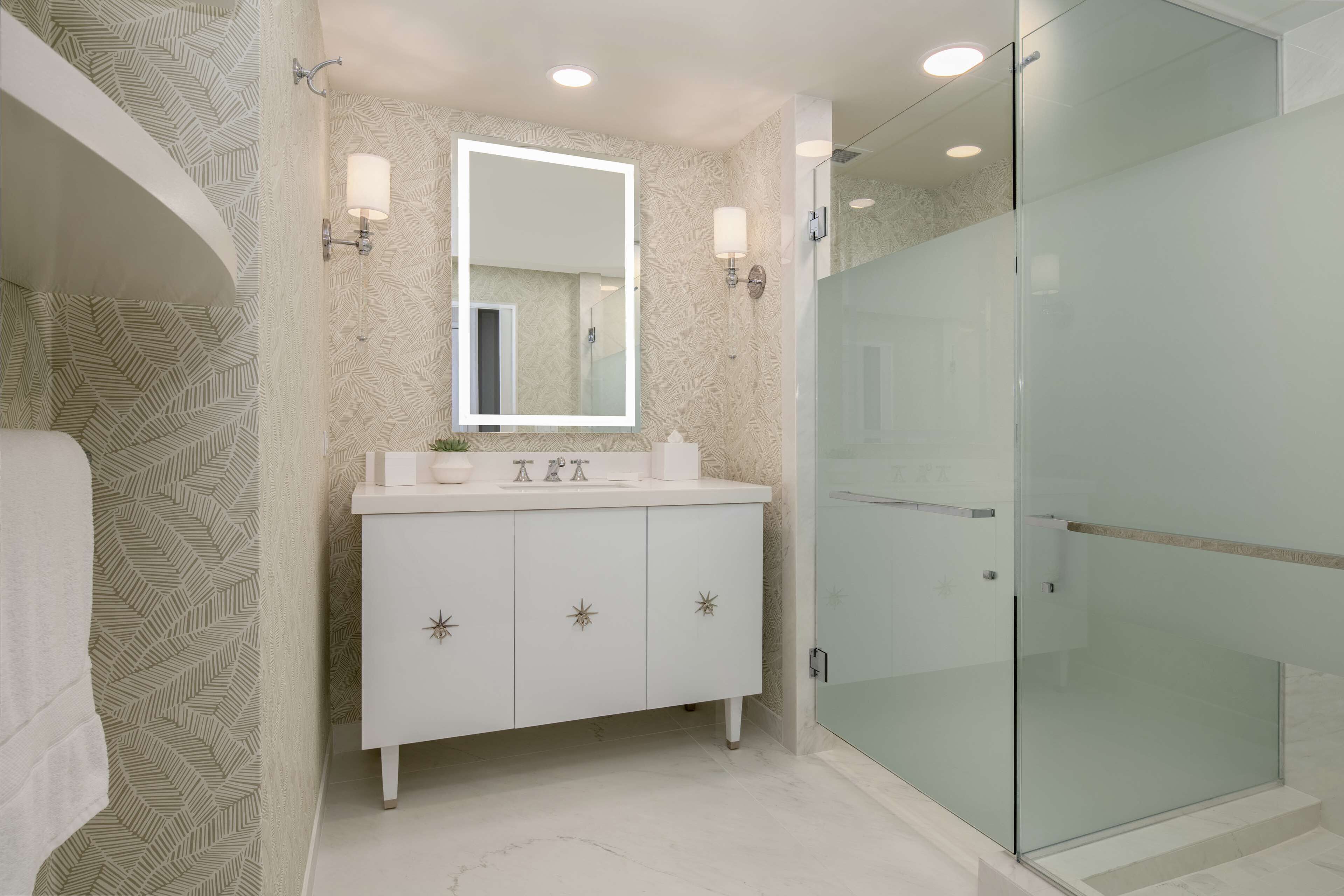 A bathroom with a white vanity, a large mirror, and a glass shower enclosure.