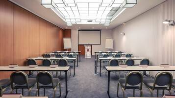 Un salón de conferencias con varias mesas y sillas, una pantalla grande y un atril.