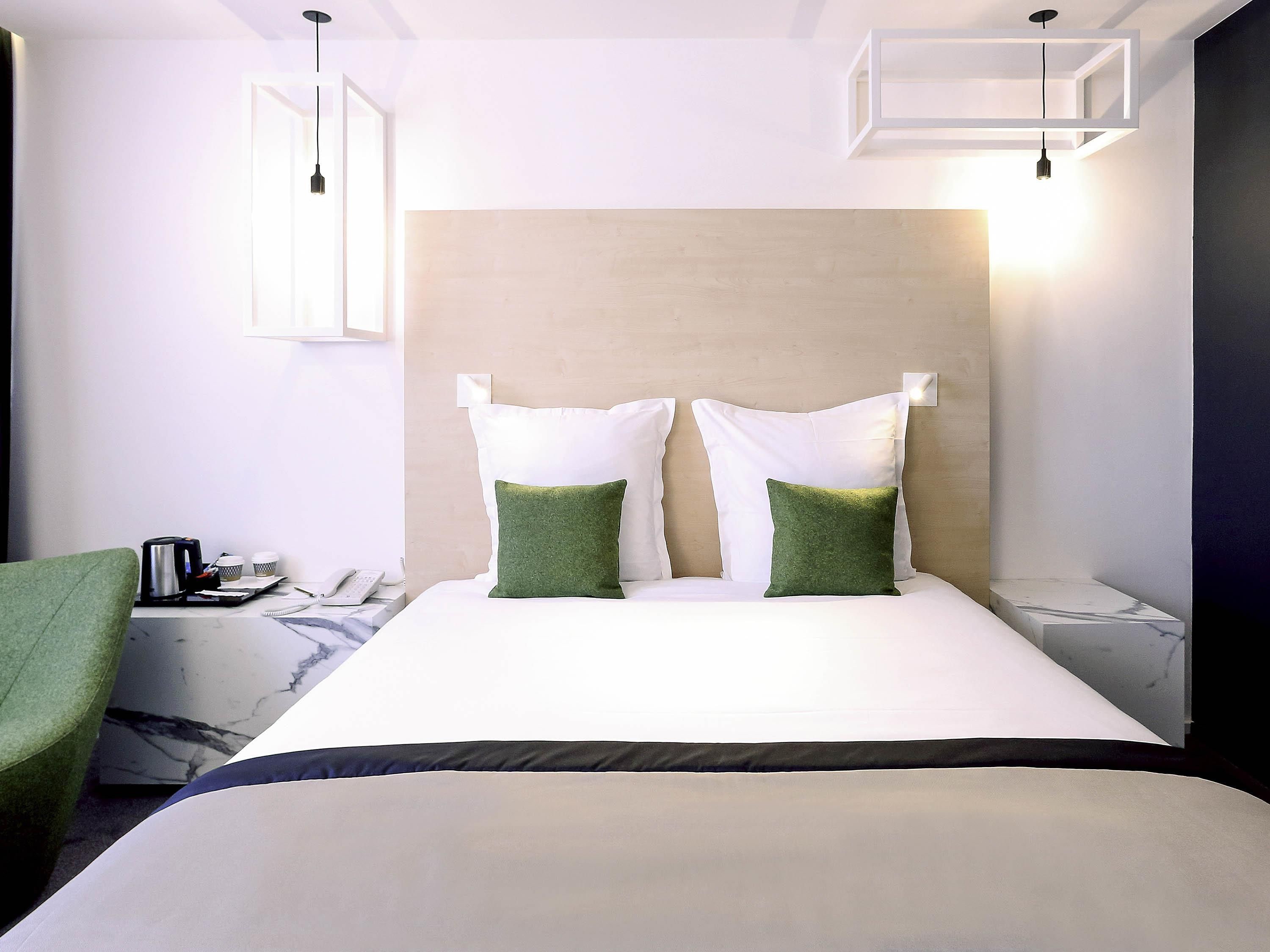 Ein Hotelzimmer mit Bett, grünem Sessel, Kaffeemaschine und Nachttisch mit Lampe.