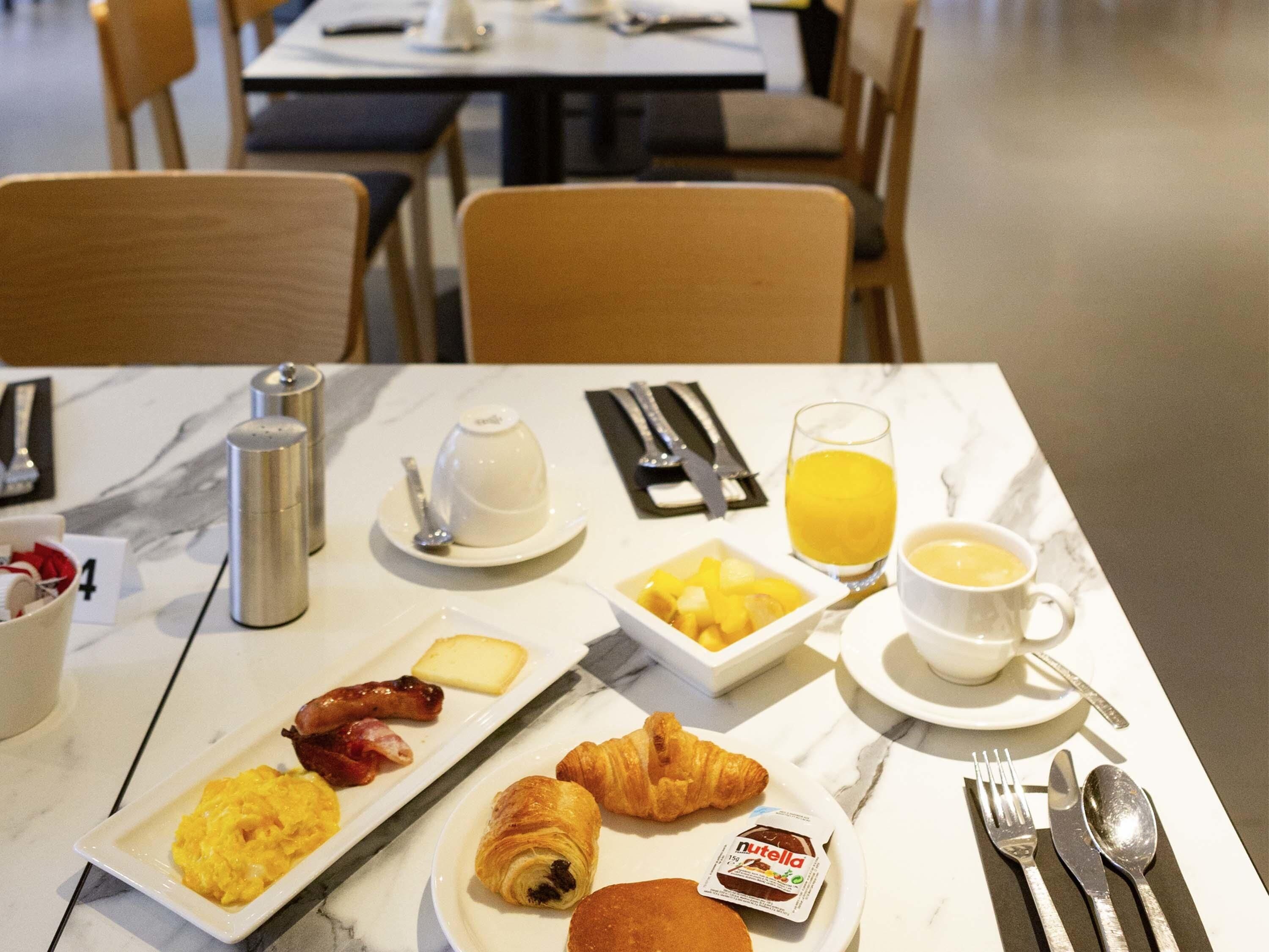 Une table de petit-déjeuner avec des assiettes remplies de nourriture, un verre de jus d’orange et une tasse de café.