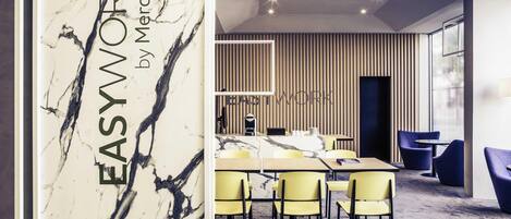 Un salón de conferencias moderno con pared de mármol, sillas amarillas, una mesa larga y un cartel que dice 'WORK'.