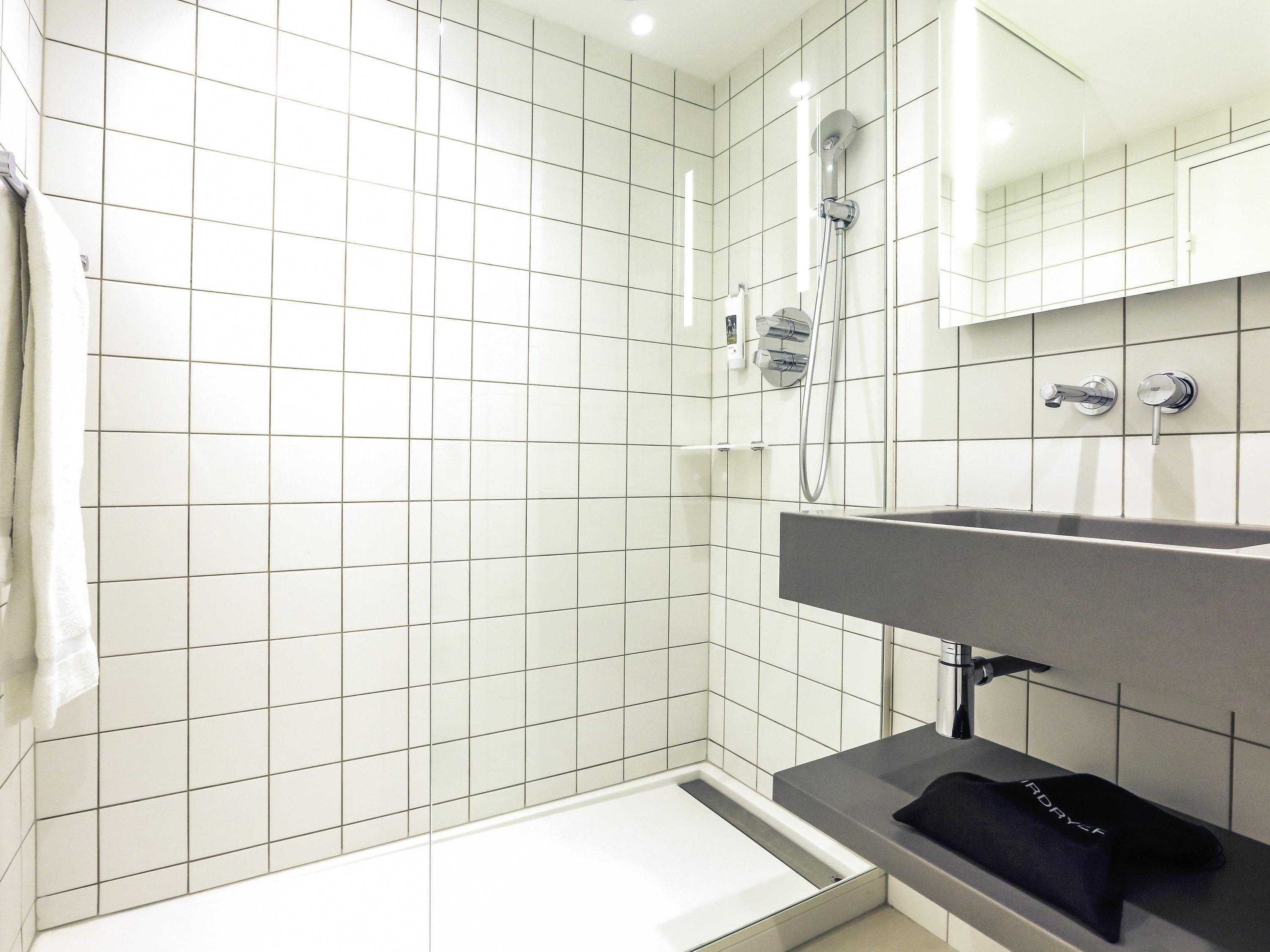 A modern bathroom with white tiled walls, a bathtub, a shower, and a vanity with a towel.