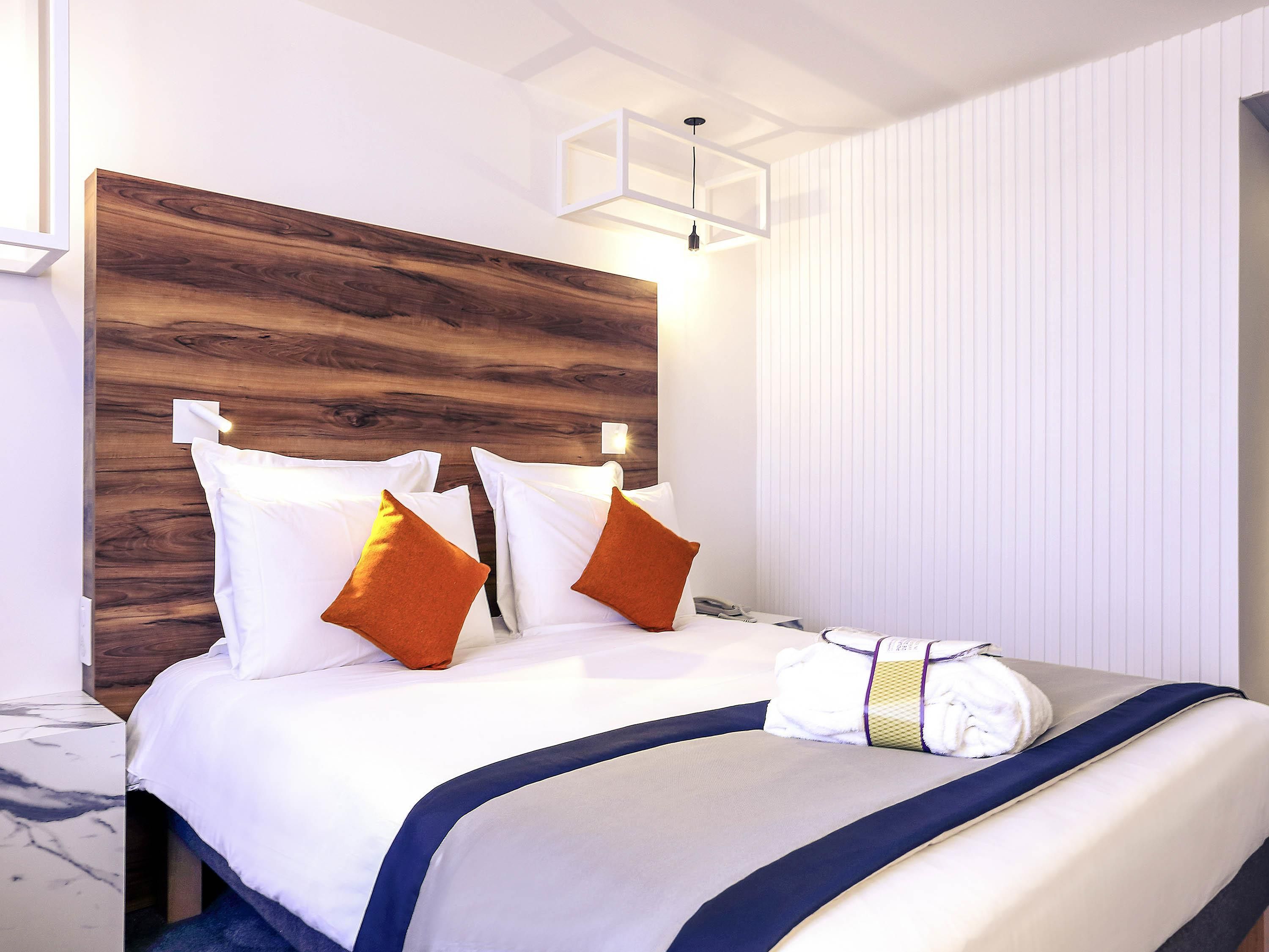 Habitación de hotel con cabecera de madera, ropa de cama blanca y mesita de noche de mármol.
