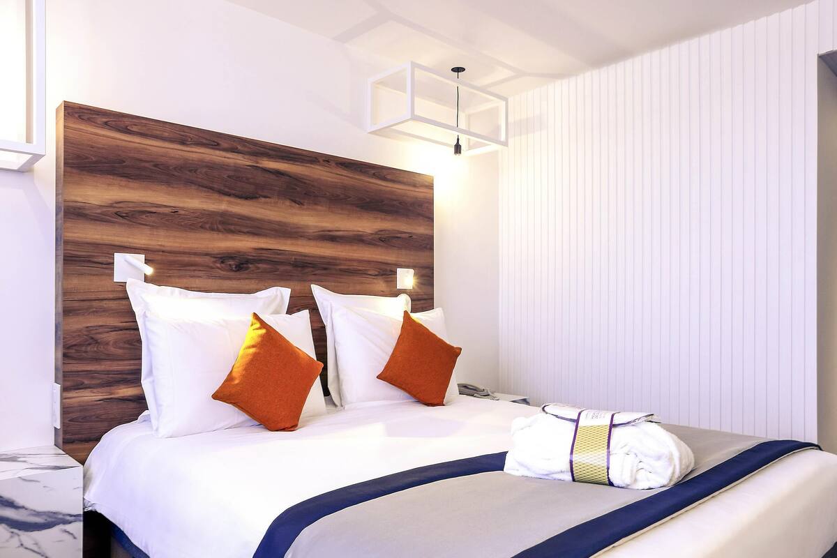 A hotel room with a wooden headboard, white bedding, and a marble nightstand.