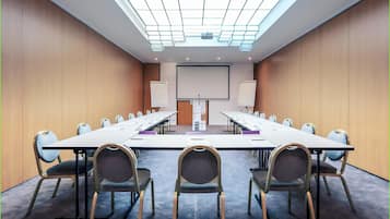 Un salón de conferencias con una larga mesa, sillas, una pantalla de proyector y una pizarra.