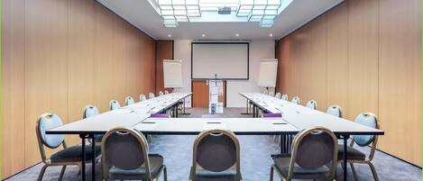 A conference room with a long table, chairs, a projector screen, and a whiteboard.