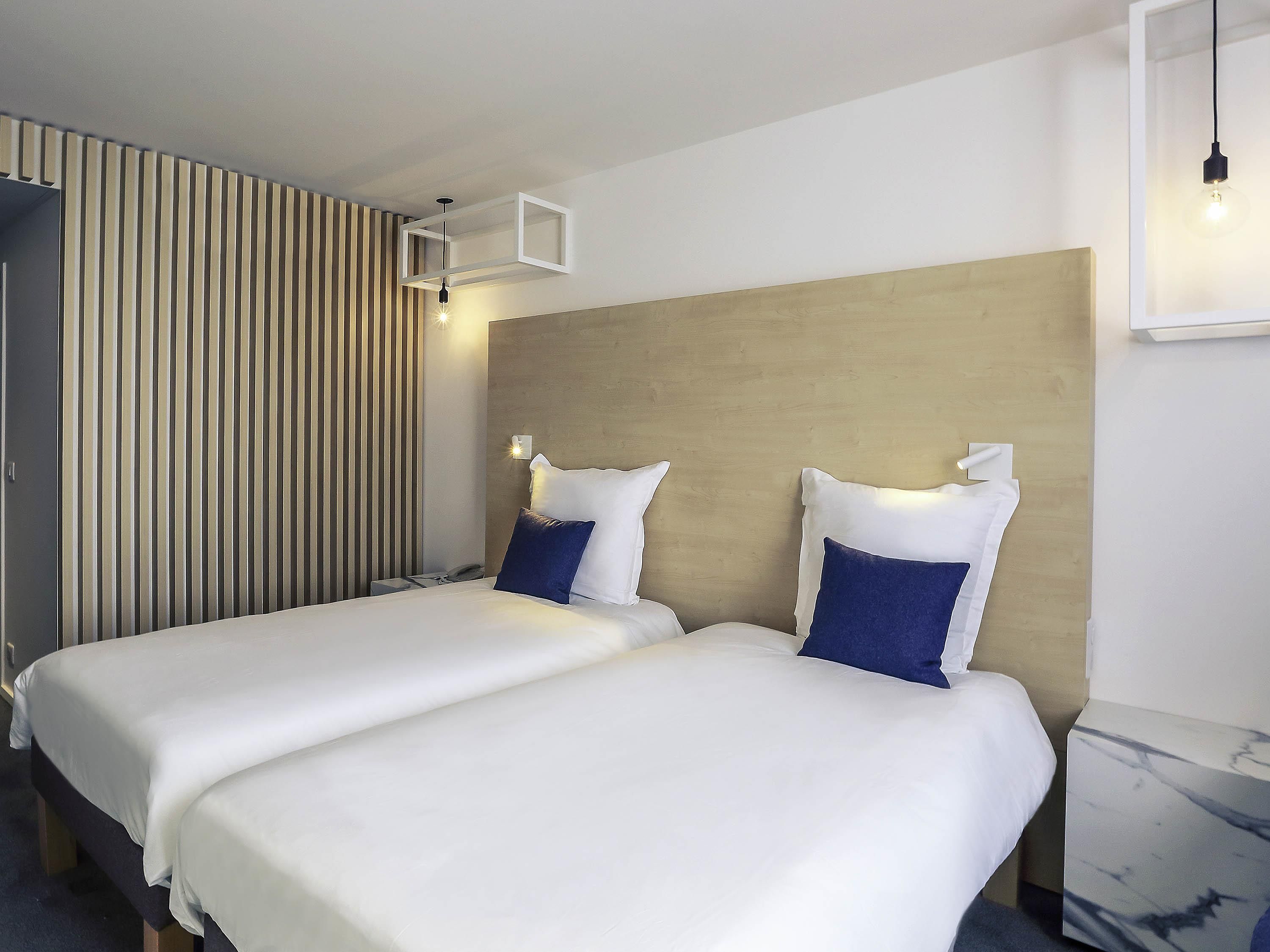 Une chambre d’hôtel avec deux lits, une tête de lit en bois et un mur à rayures.