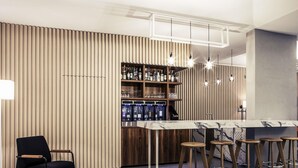 Uma área de bar moderna com bancada de mármore, banquetas de madeira e parede de ripas de madeira verticais.